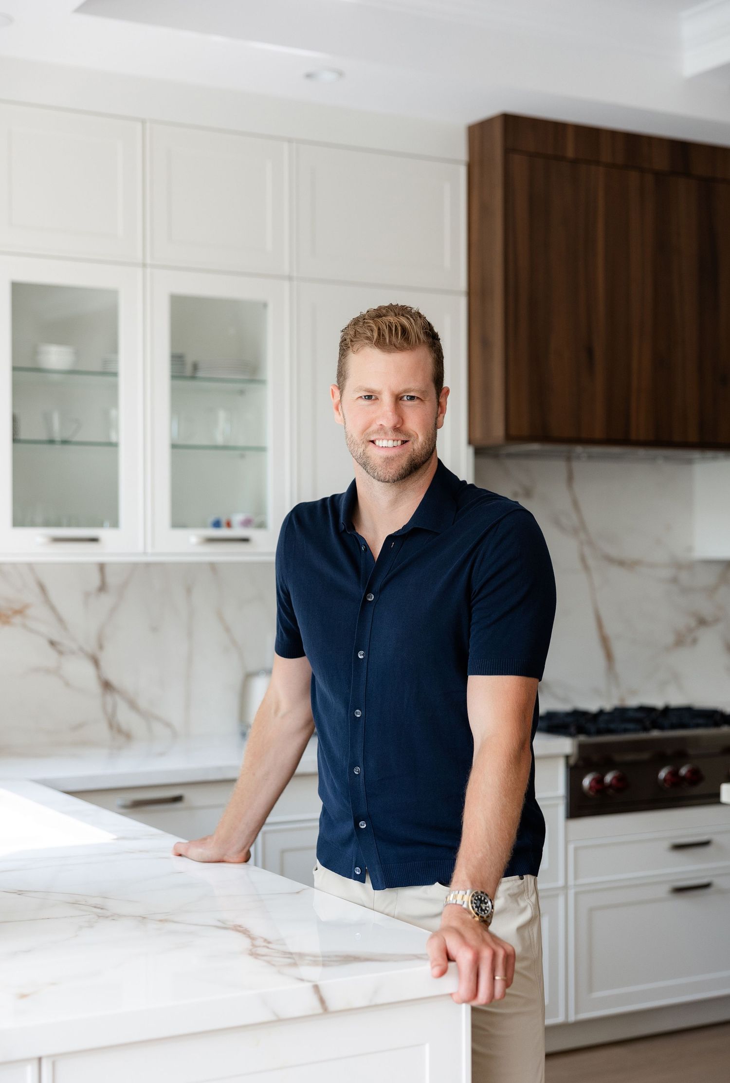 Man in navy polo shirt stands at white marble kitchen counter.