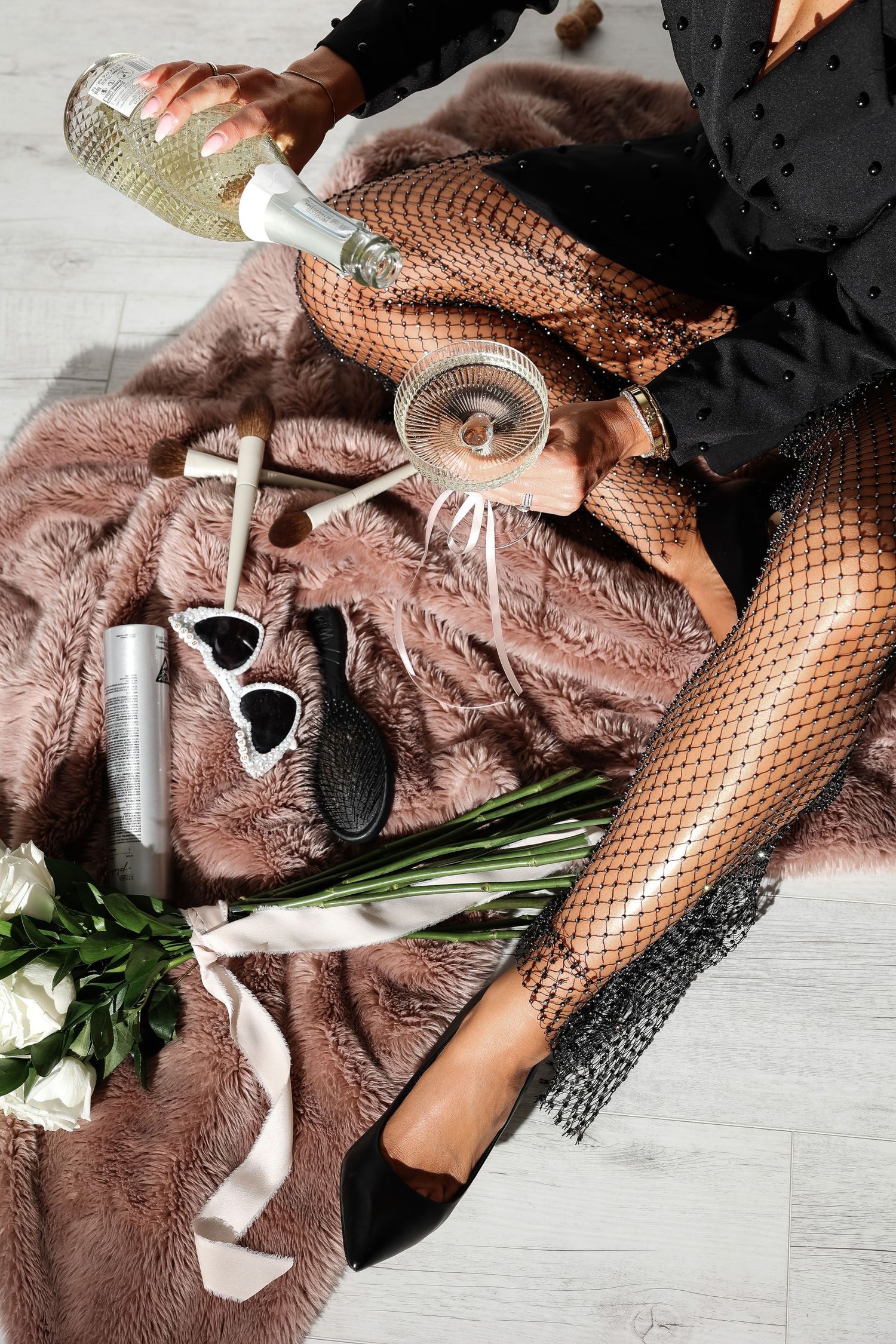 Artistic flat lay with fishnet stockings, flowers, and accessories on pink fabric.