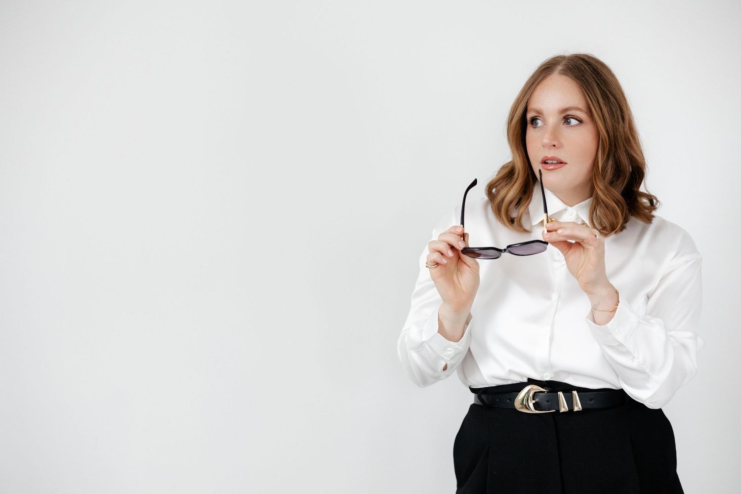 Casual pose holding sunglasses while wearing classic white and black ensemble.