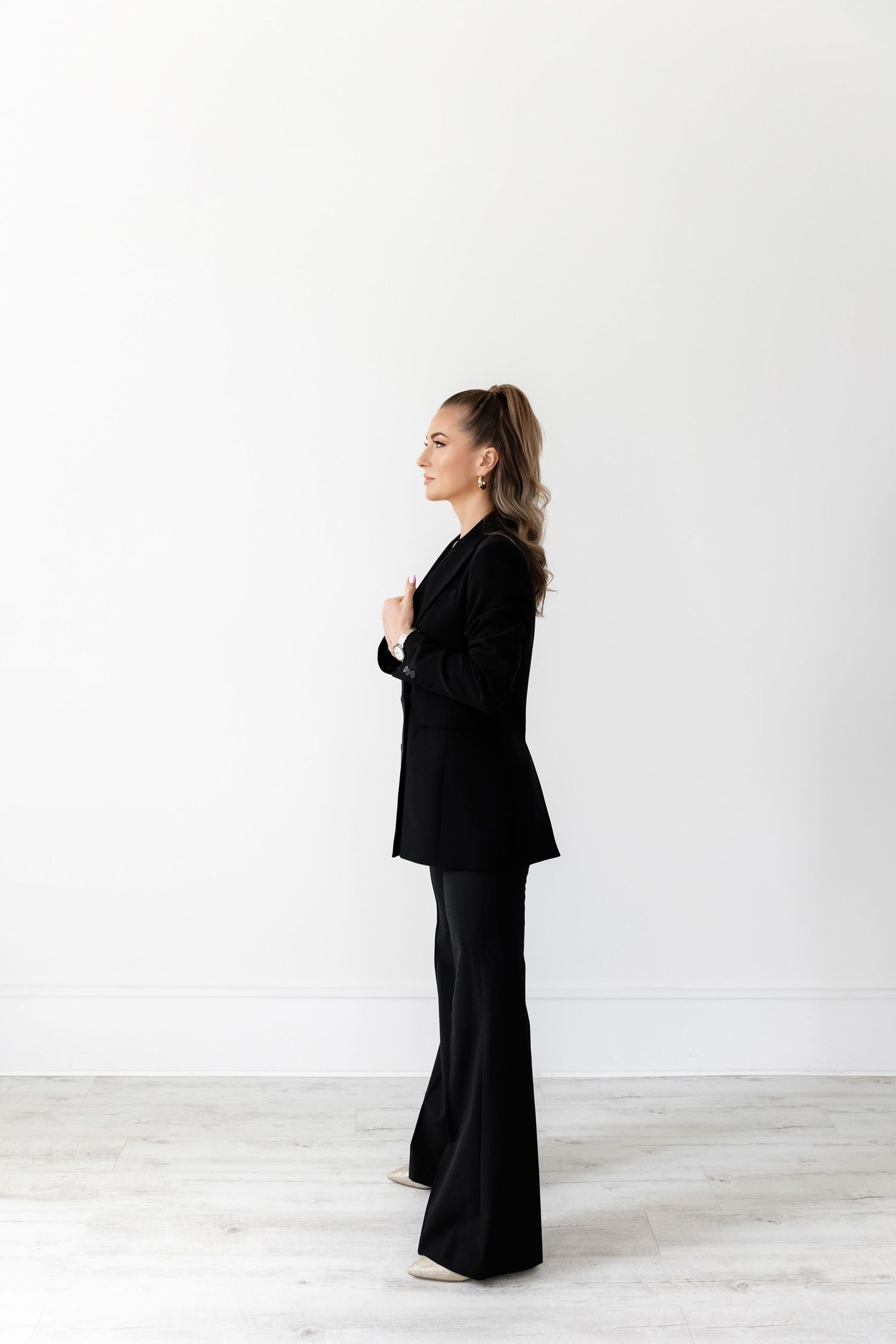 Side profile of woman in black suit standing confidently against white background.