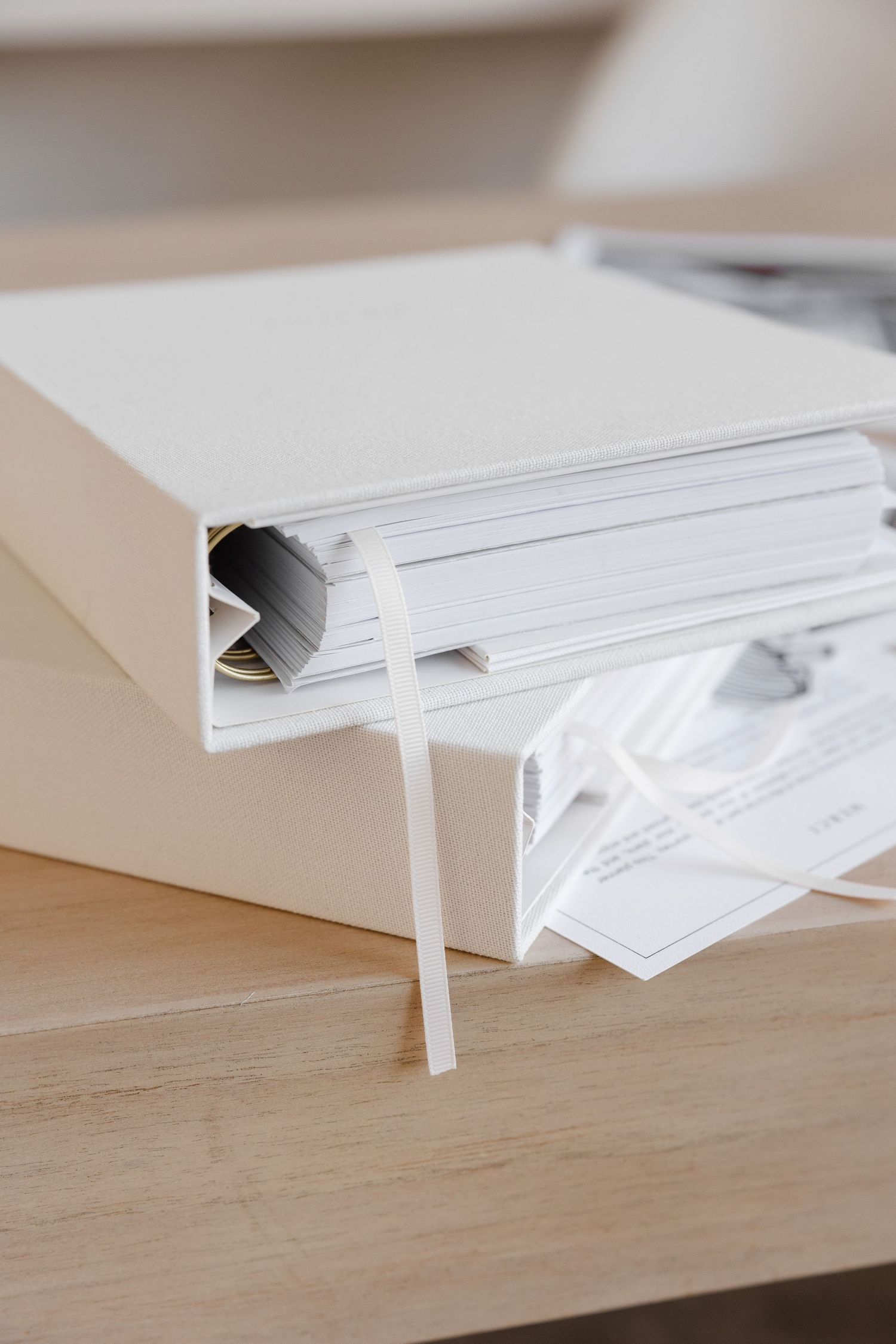 Close-up of white binder with ribbon bookmark on wooden desk surface.