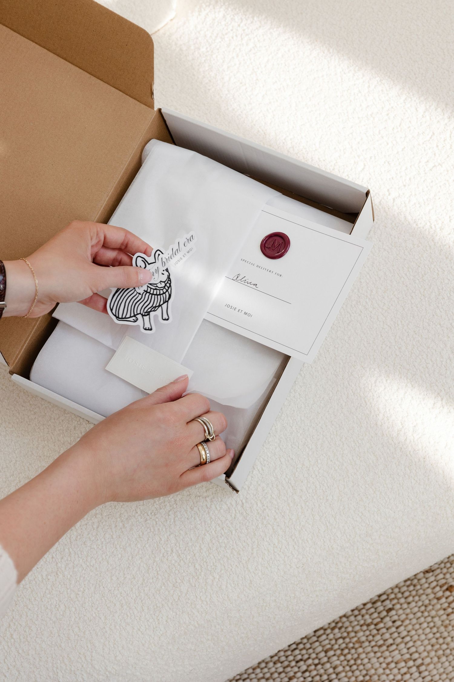 Hands revealing contents of branded white box with zebra logo and wax seal.