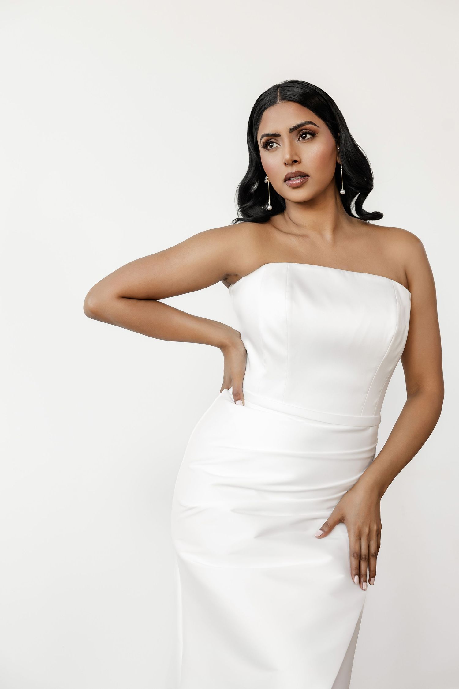 Modern bridal portrait in structured white strapless gown against white backdrop.