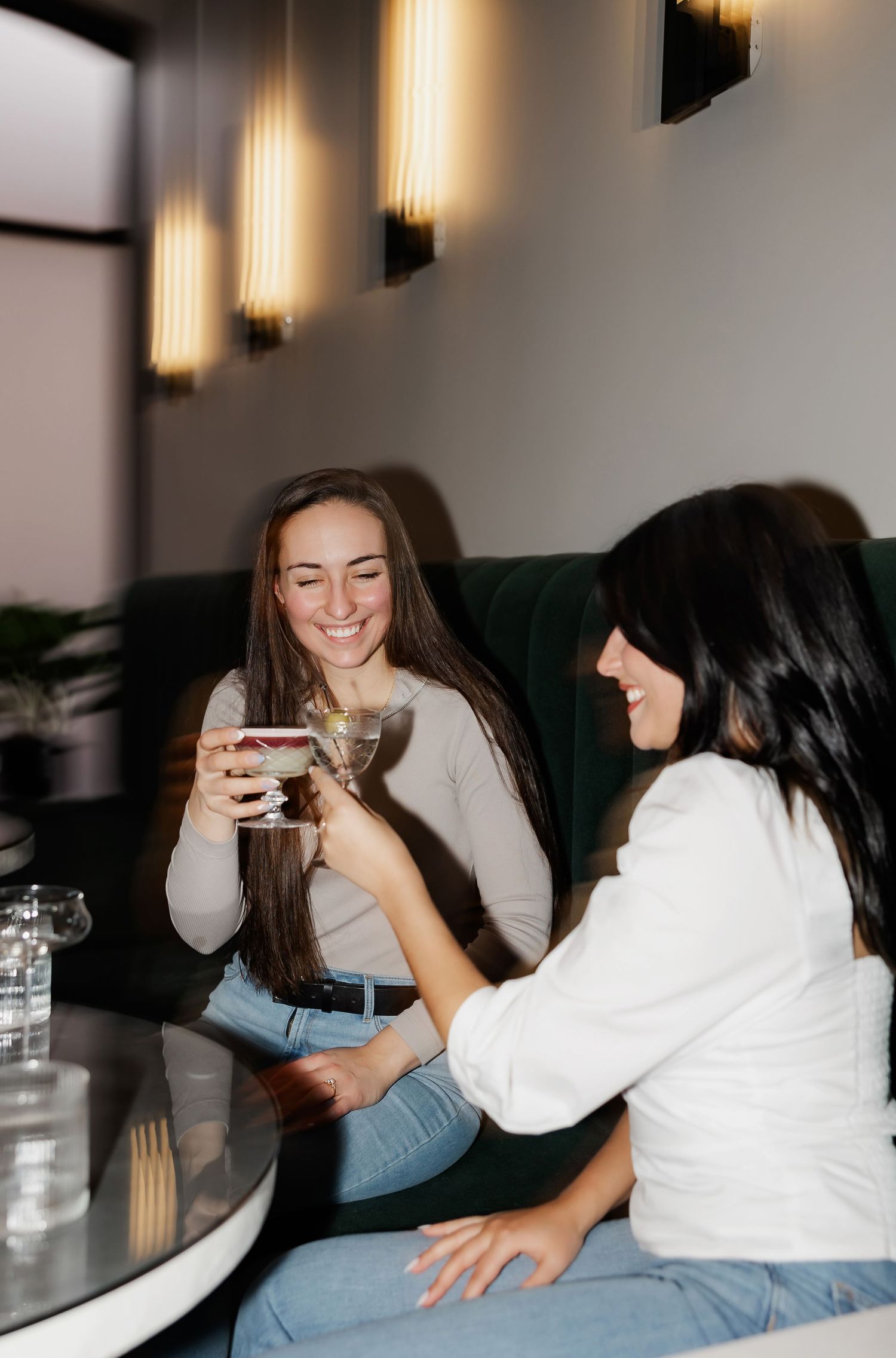 Friends enjoying drinks and laughing together on a couch in a cozy setting.