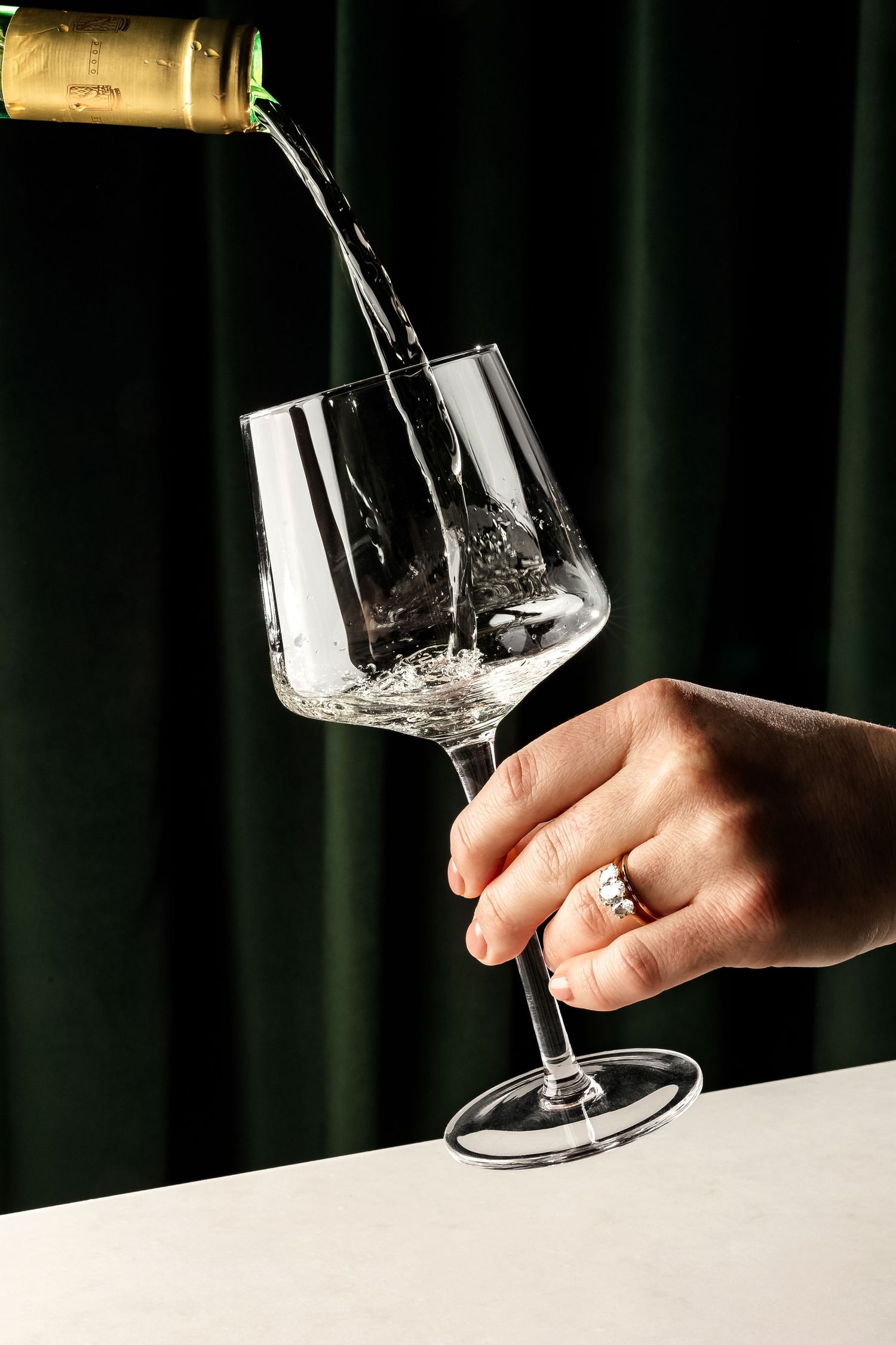 White wine being poured into a crystal glass against a dark green velvet backdrop.