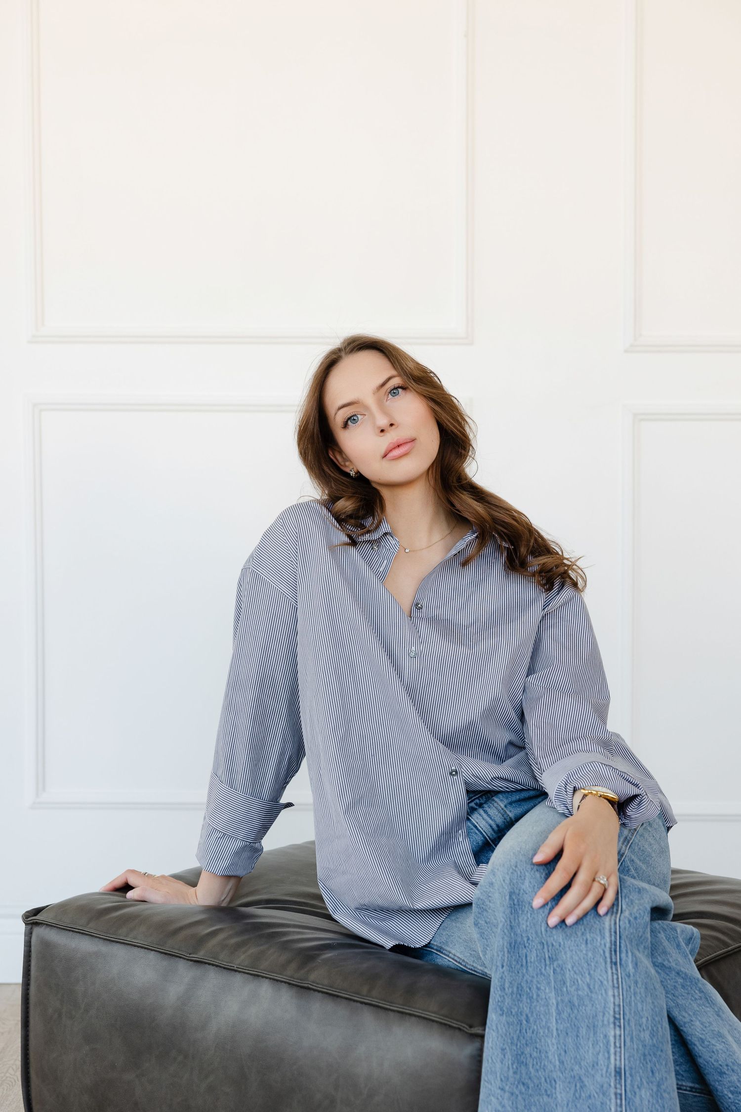 Casual portrait on leather ottoman wearing oversized grey button-down and jeans.