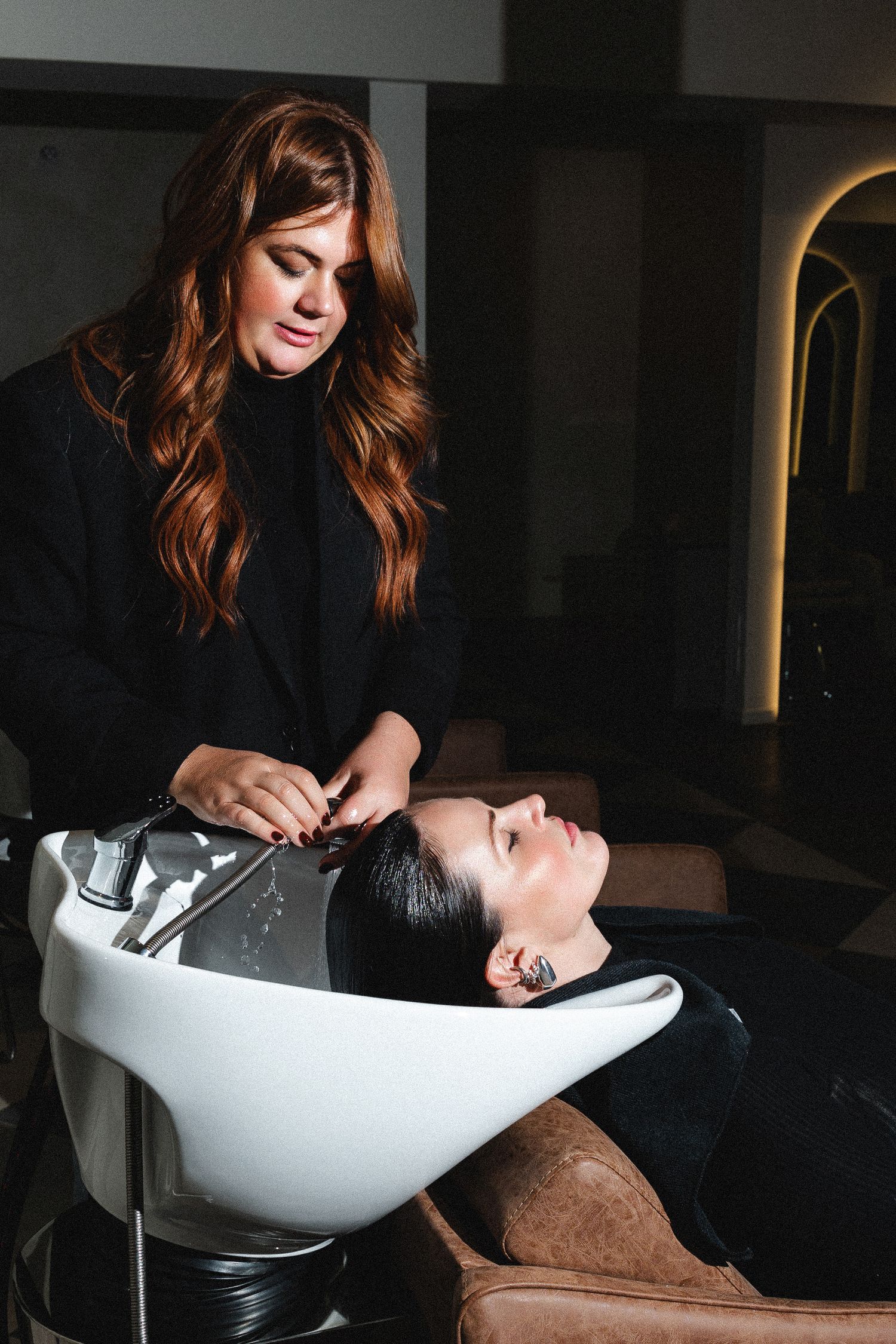 Hair washing station with white basin and dark interior salon setting.