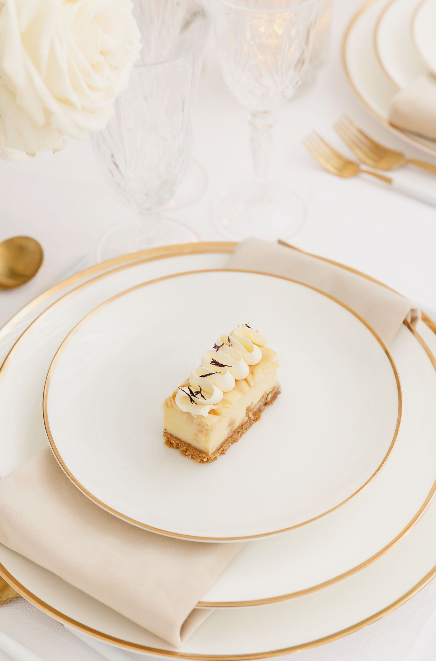 Sophisticated dining setup with gold-rimmed plates and small dessert bites on white dinnerware.