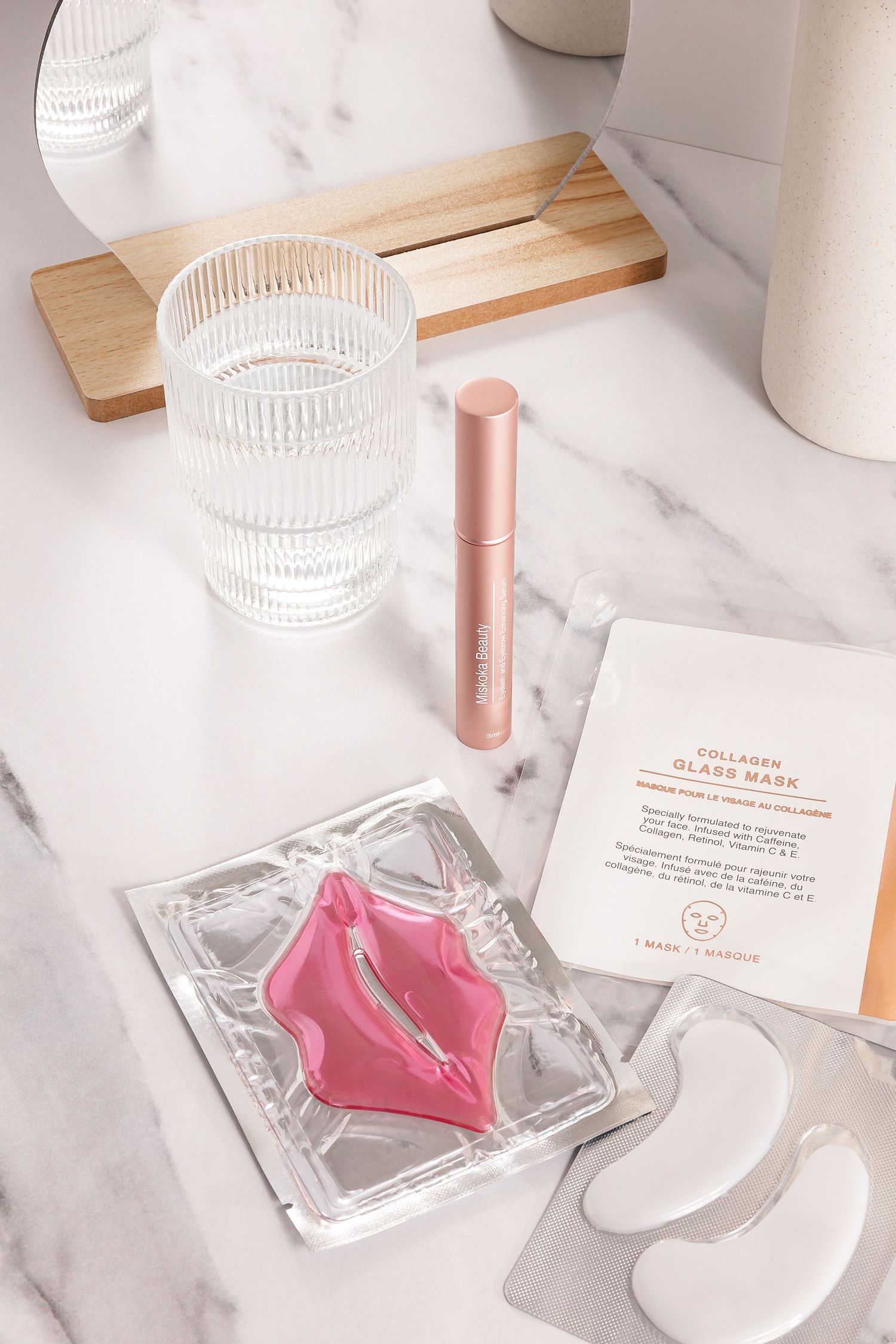 Pink lip masks and beauty products arranged on marble surface with glass accessories.