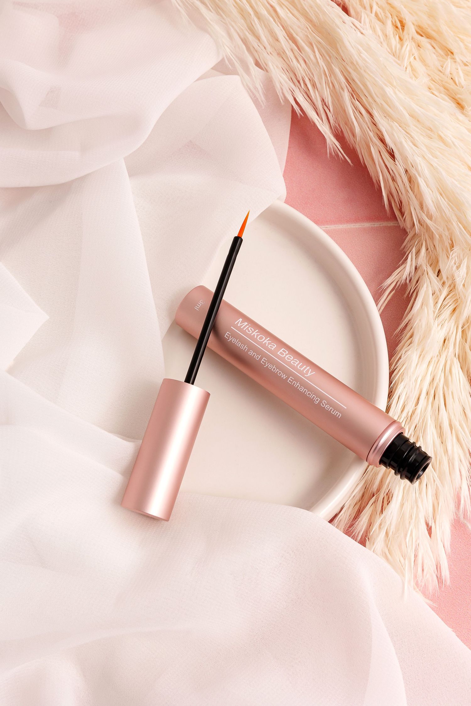 Rose gold mascara or brow product wand against white fabric background.