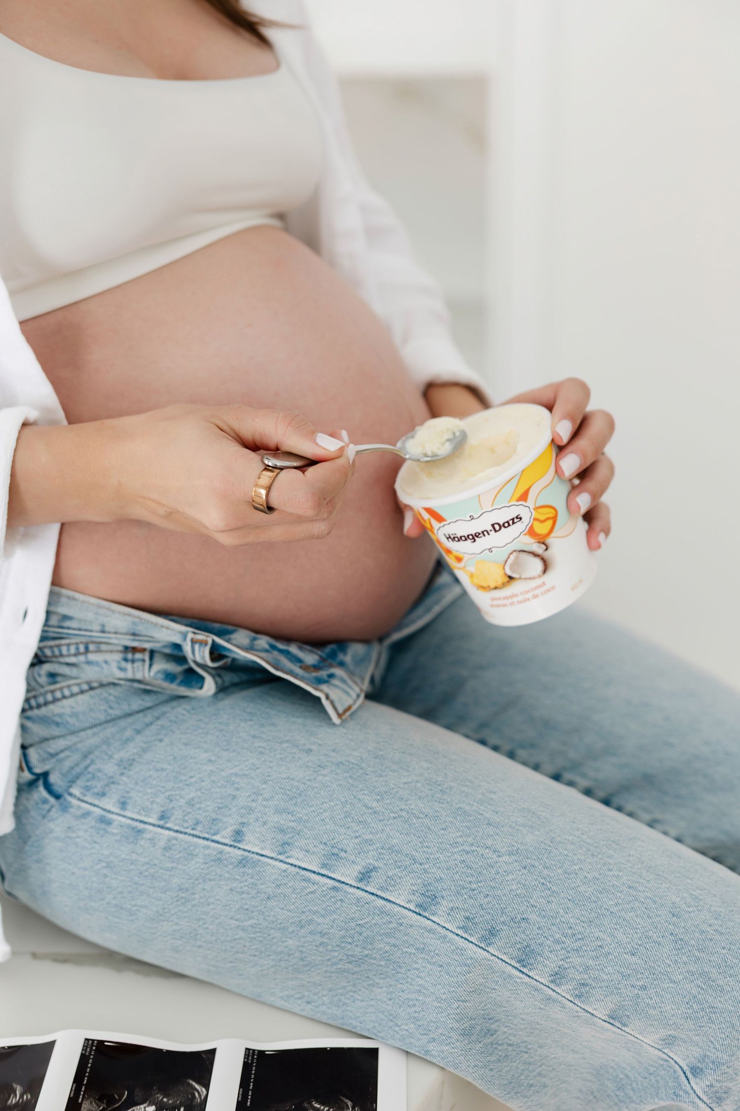 Close-up of pregnant belly while holding small snack container in modern kitchen.