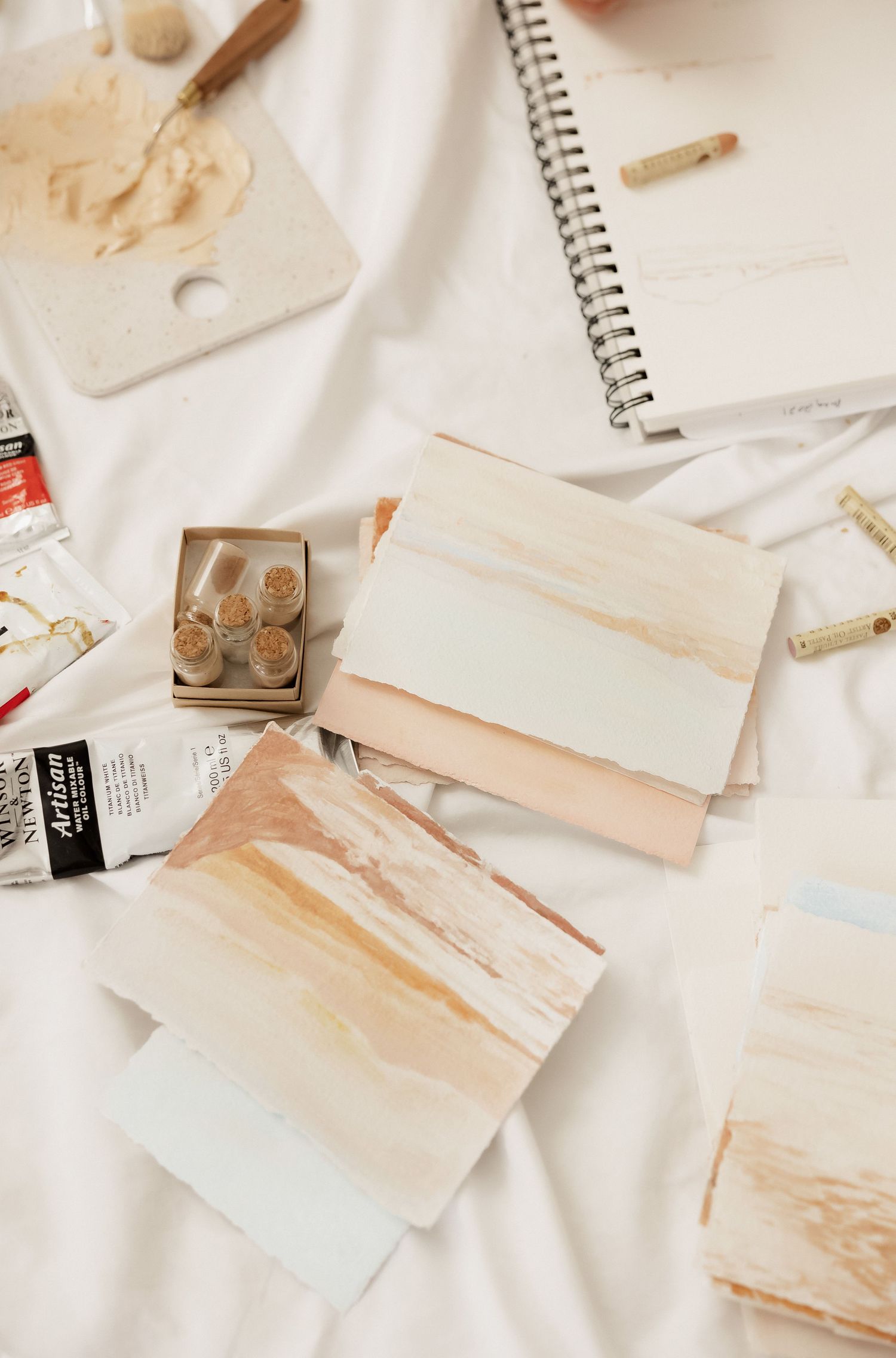 Overhead view of art supplies and notebooks with watercolor stains on white surface.