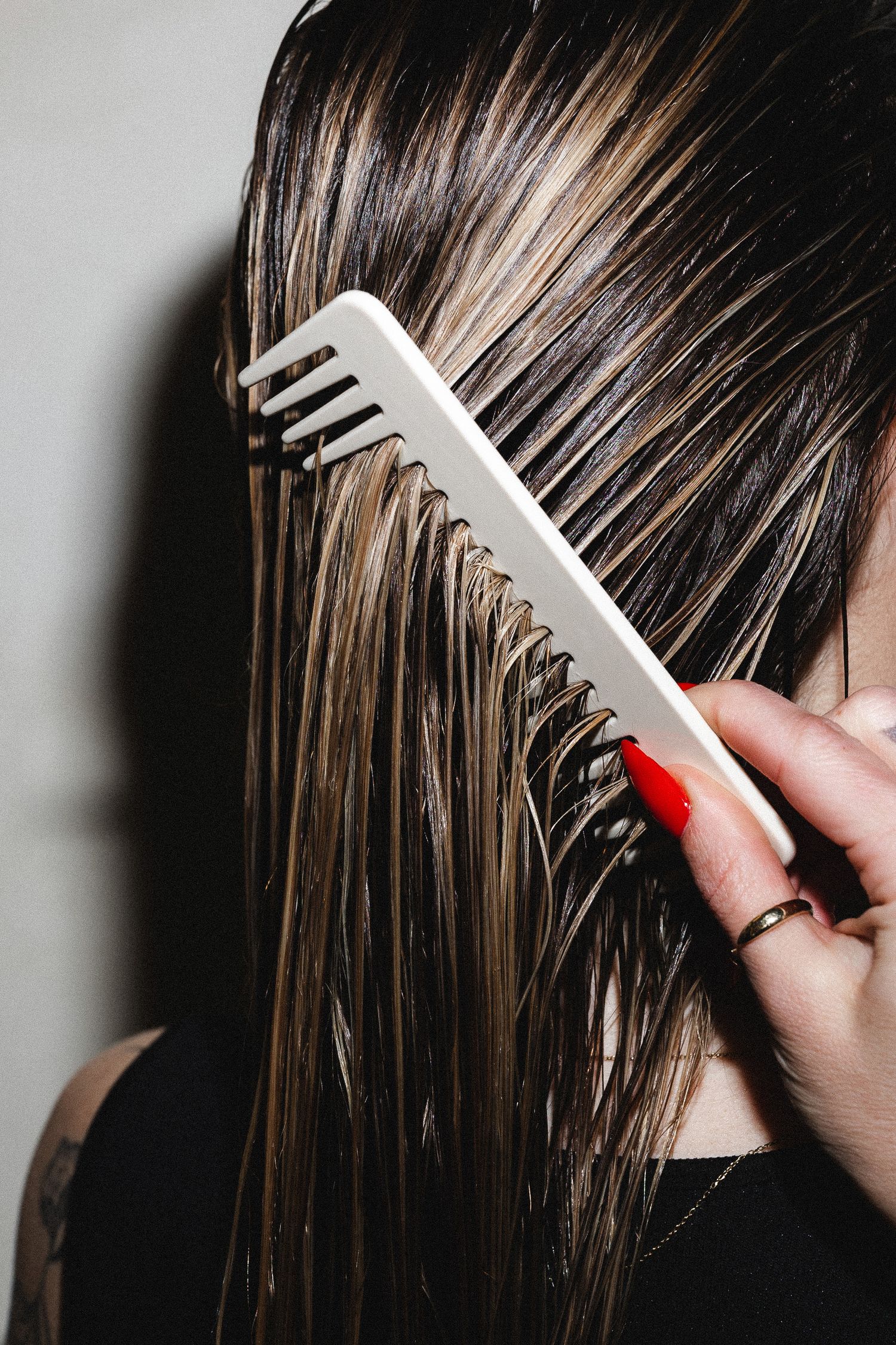 Wide-toothed comb being drawn through wet dark hair.