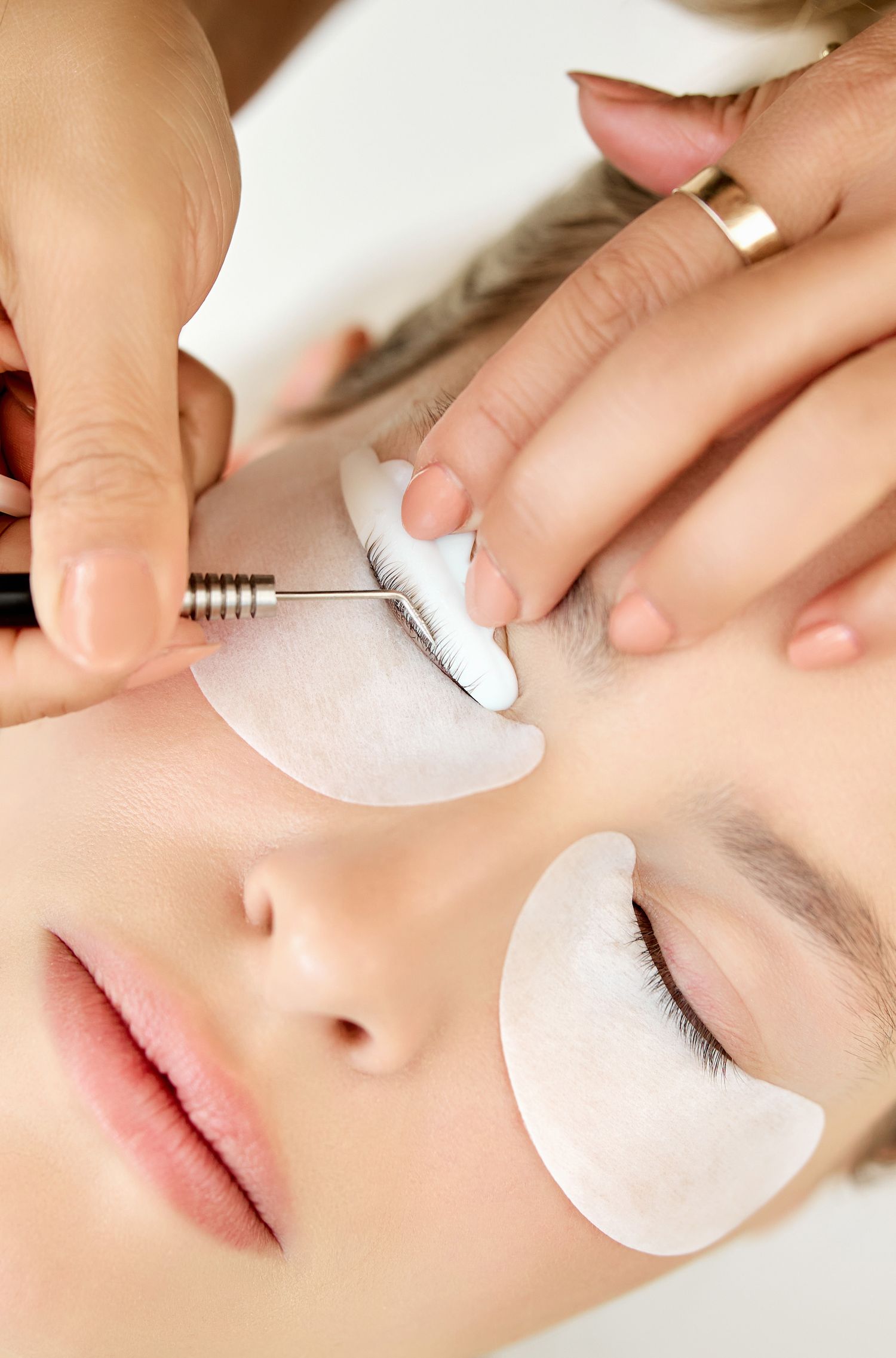 Professional applying individual eyelash extensions with specialized tweezers and tools.