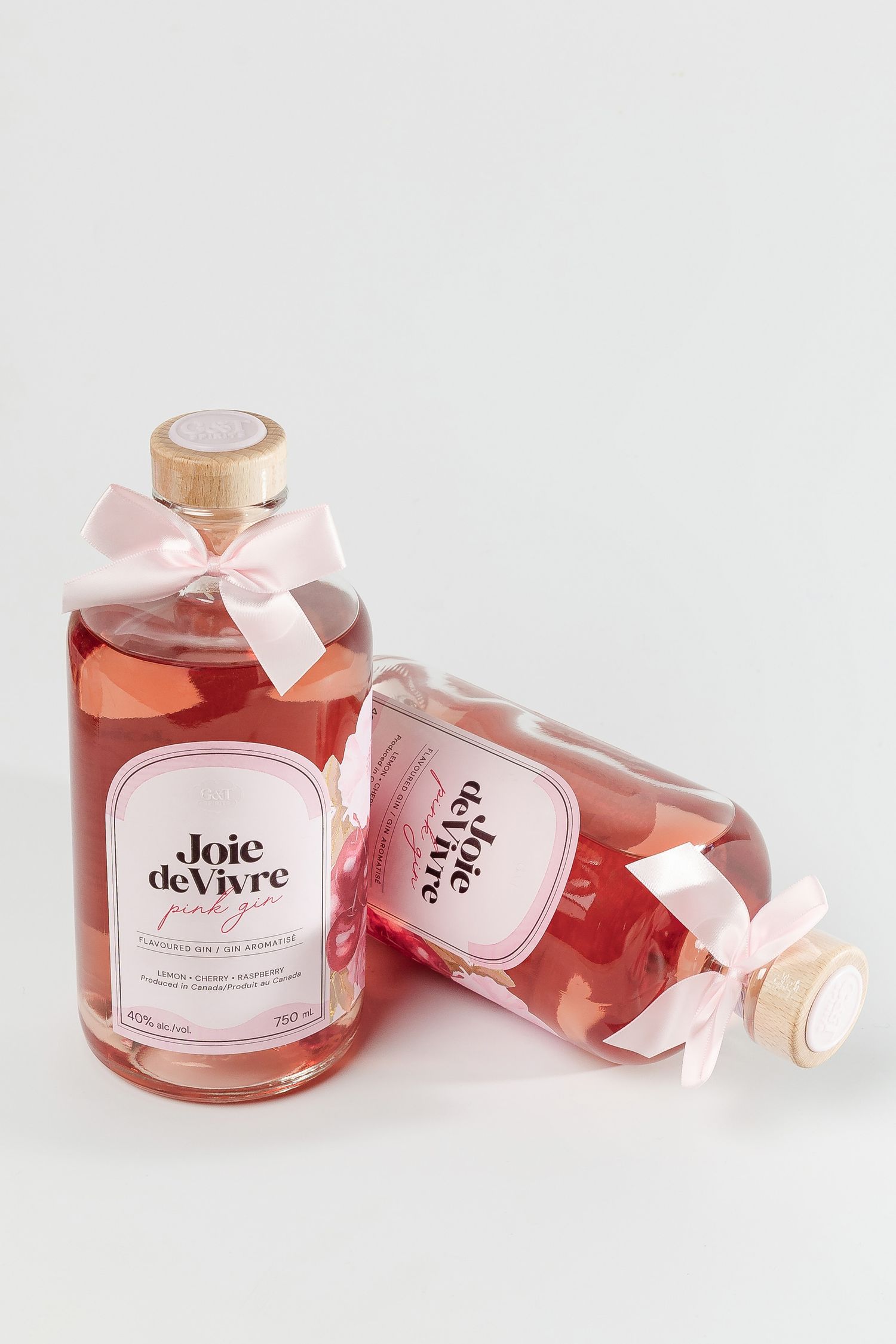 Elegant pink wine bottles with white ribbons and 'Joie de Vivre' labels arranged artistically on white background.