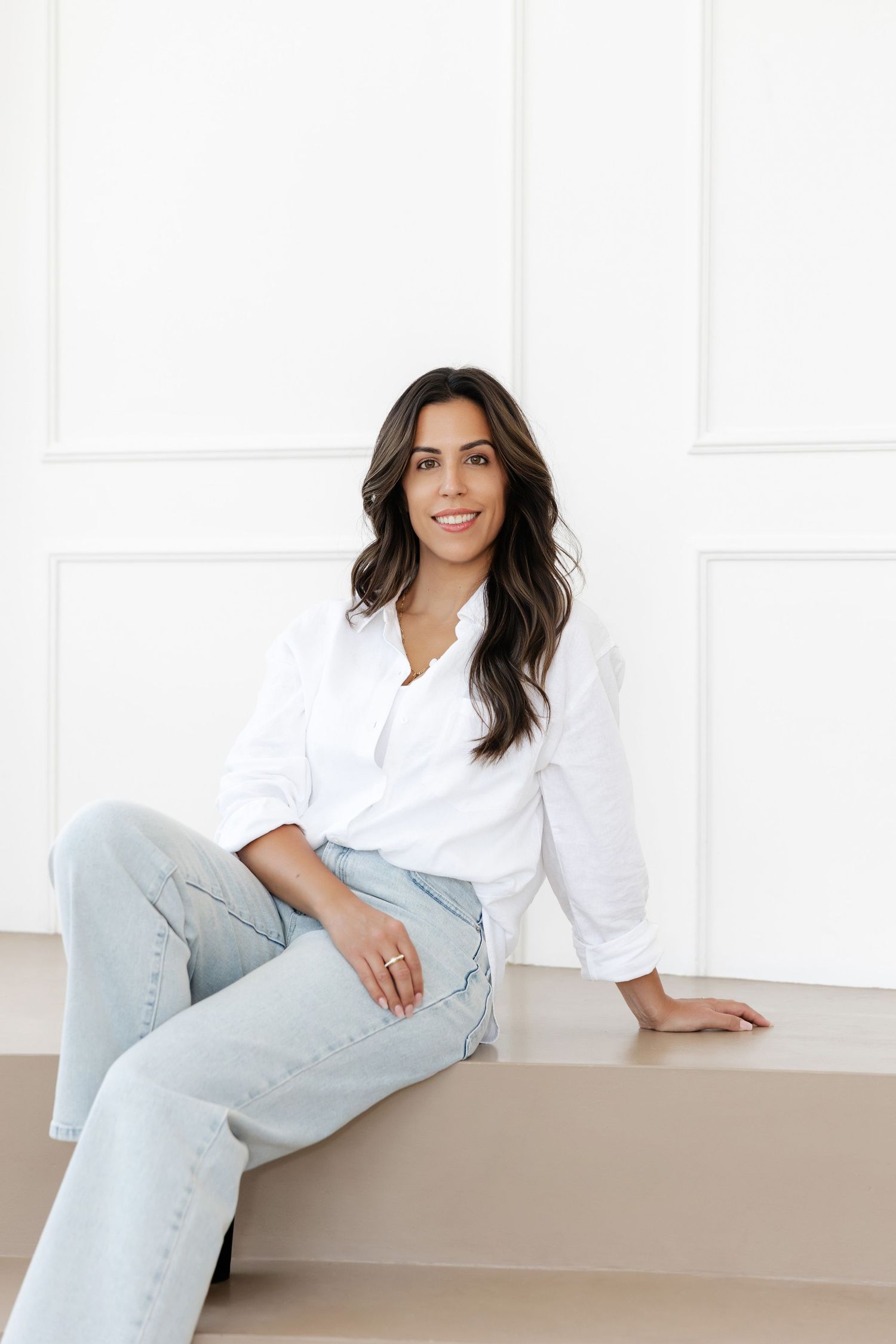 Person in casual business attire relaxes on built-in seating in bright white room.