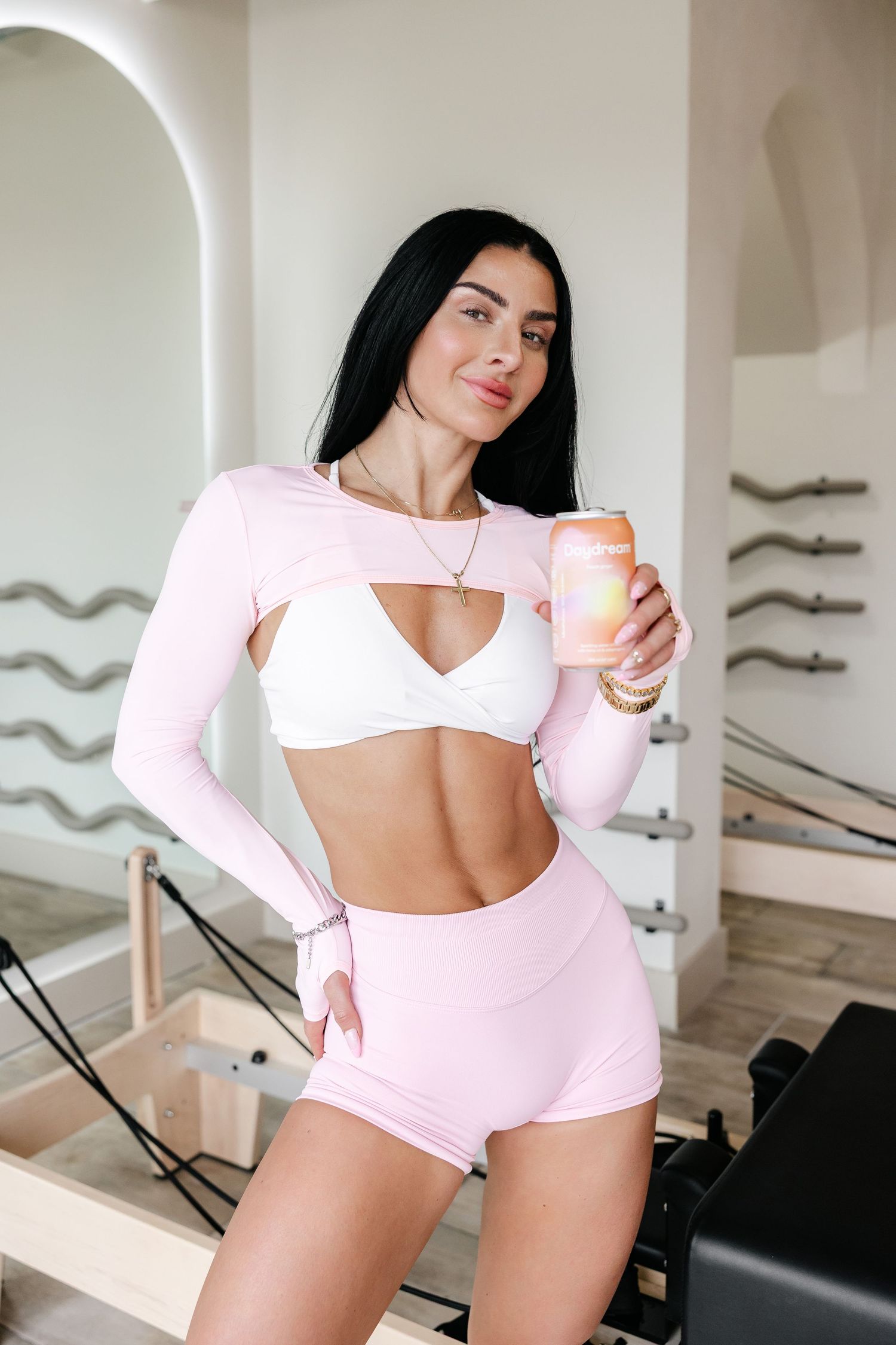Athletic figure in pink and white workout attire posing in a bright fitness studio.