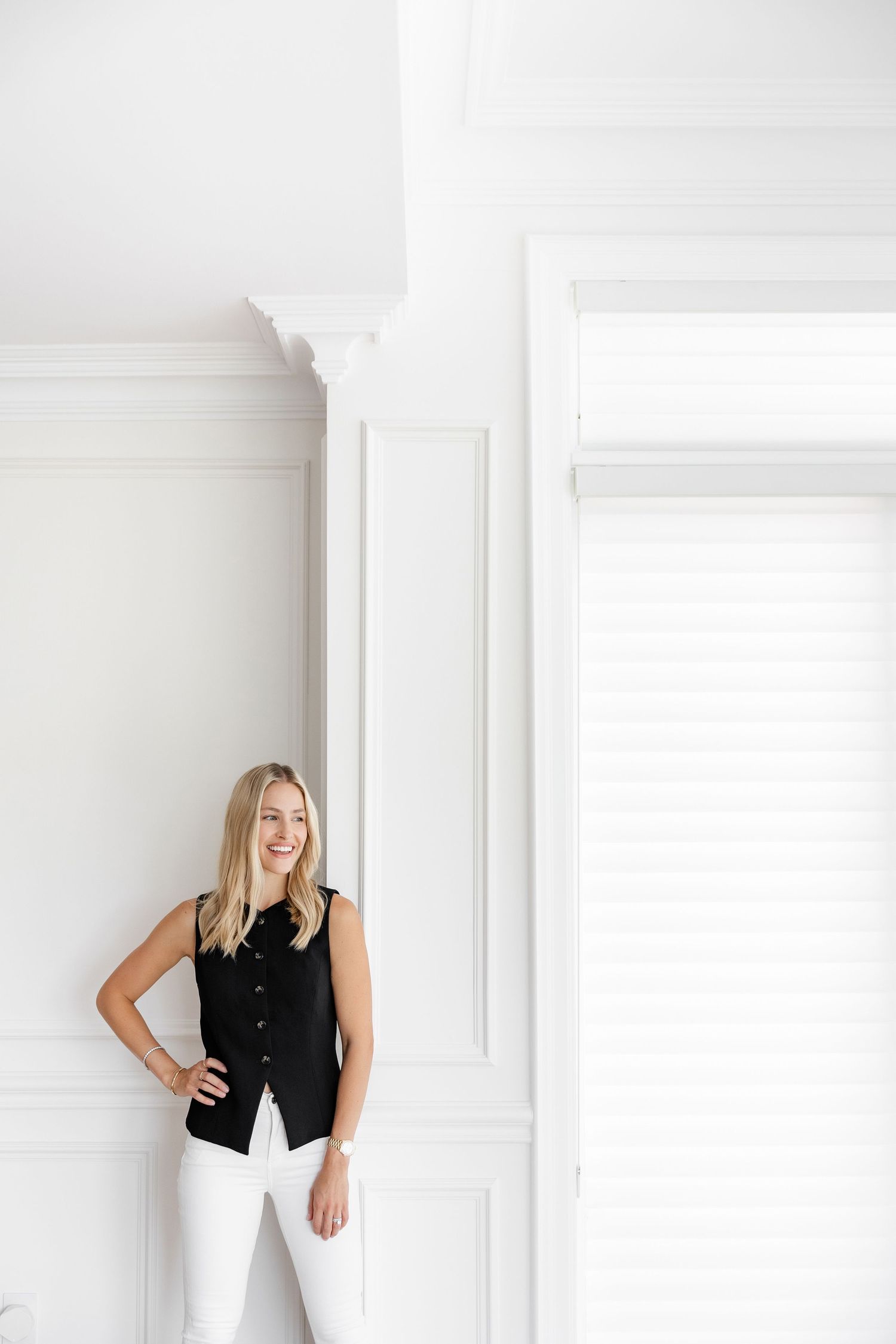 Professional portrait of person in black vest and white pants against bright interior wall.