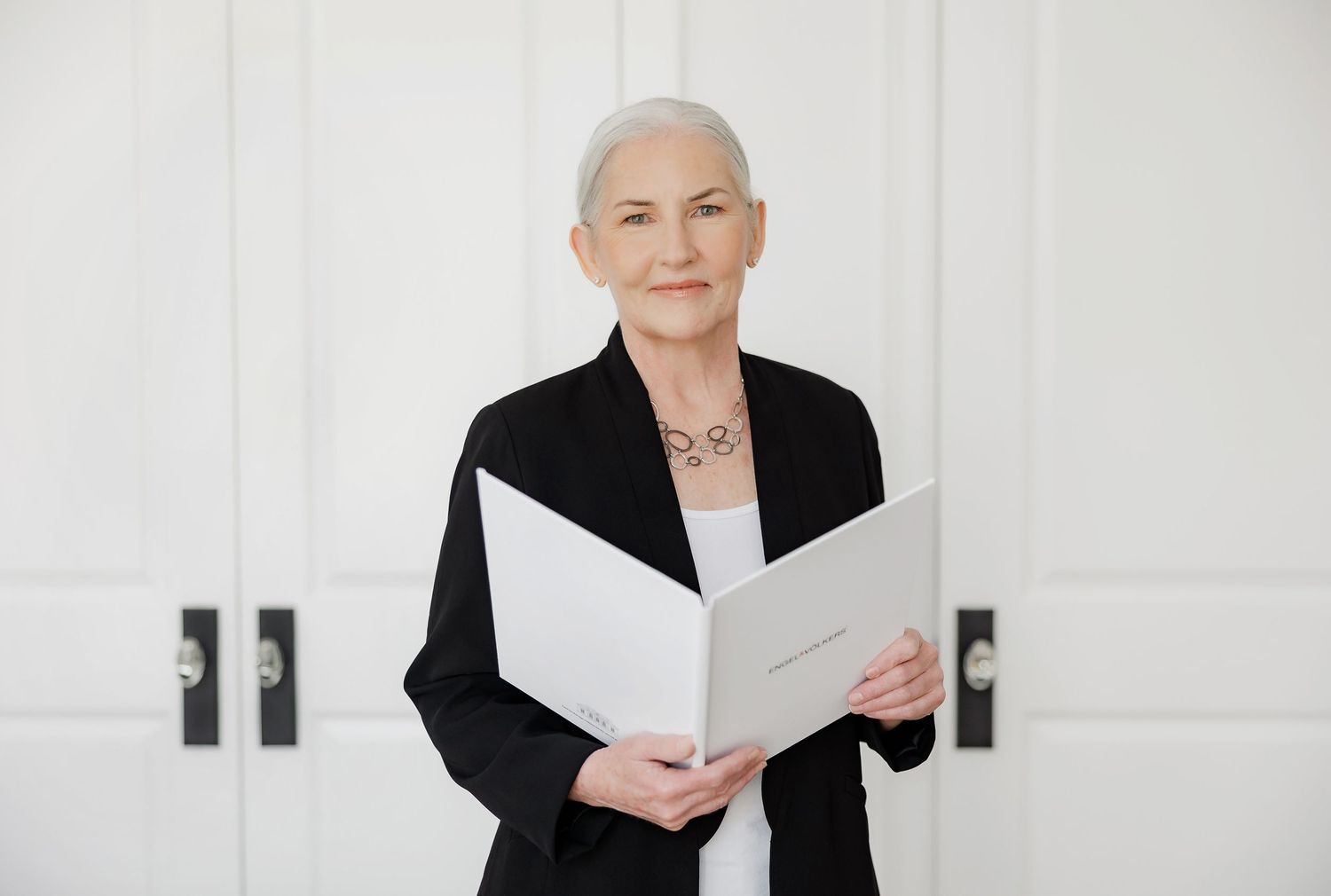 Professional in black blazer reviews documents while standing against white doors.