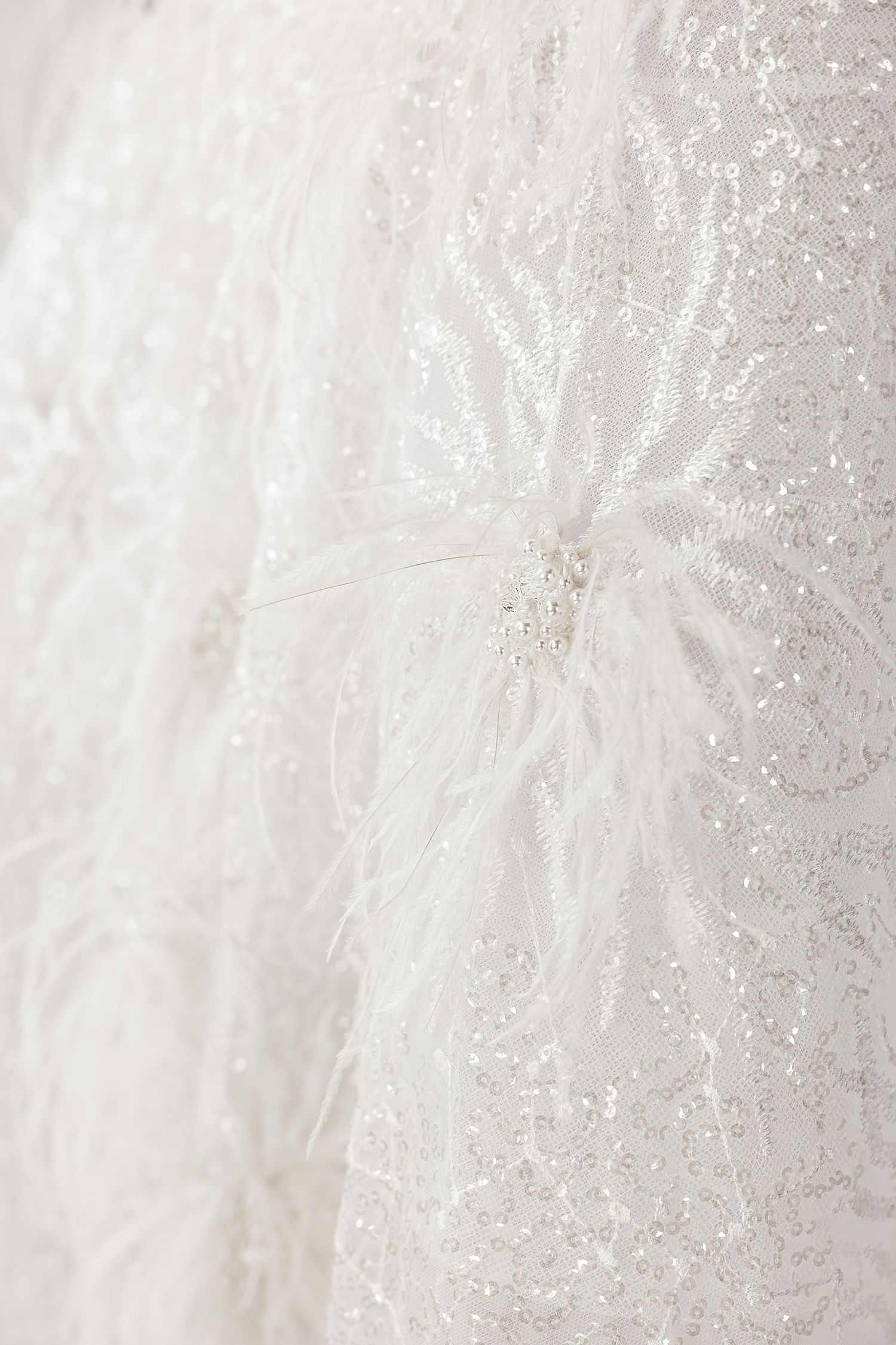 Intricate white lace and beading detail of a wedding dress fabric shown in close-up.