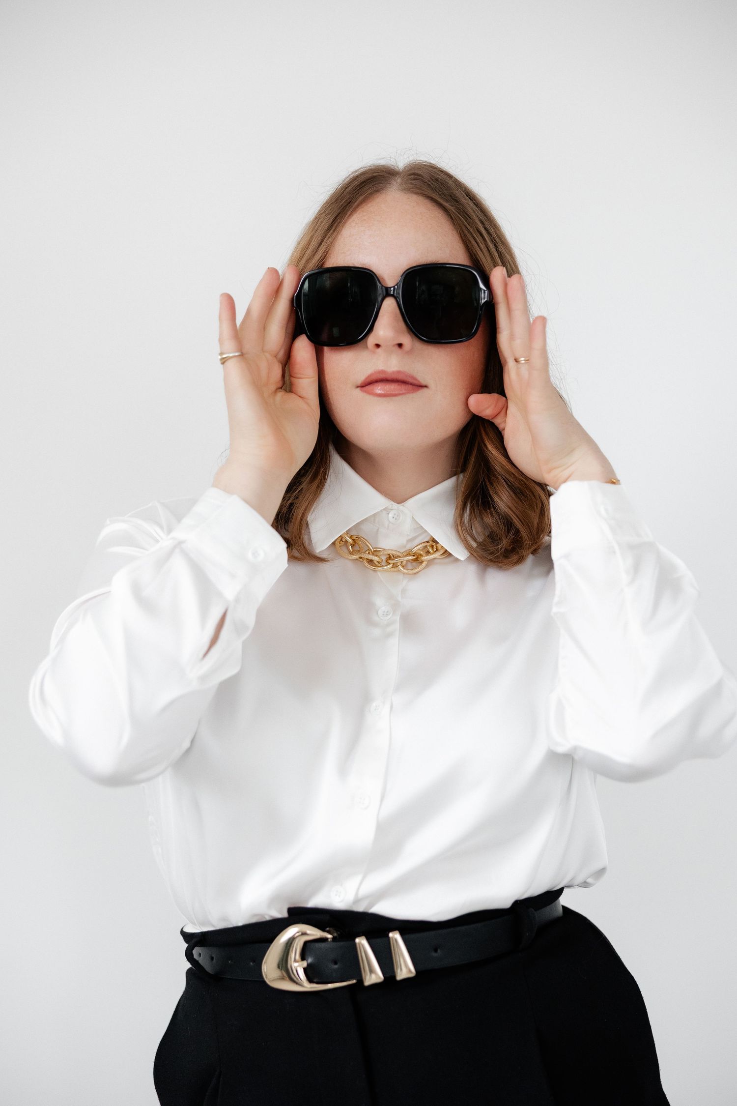 Fashion portrait showing sunglasses styled with white blouse and statement belt.