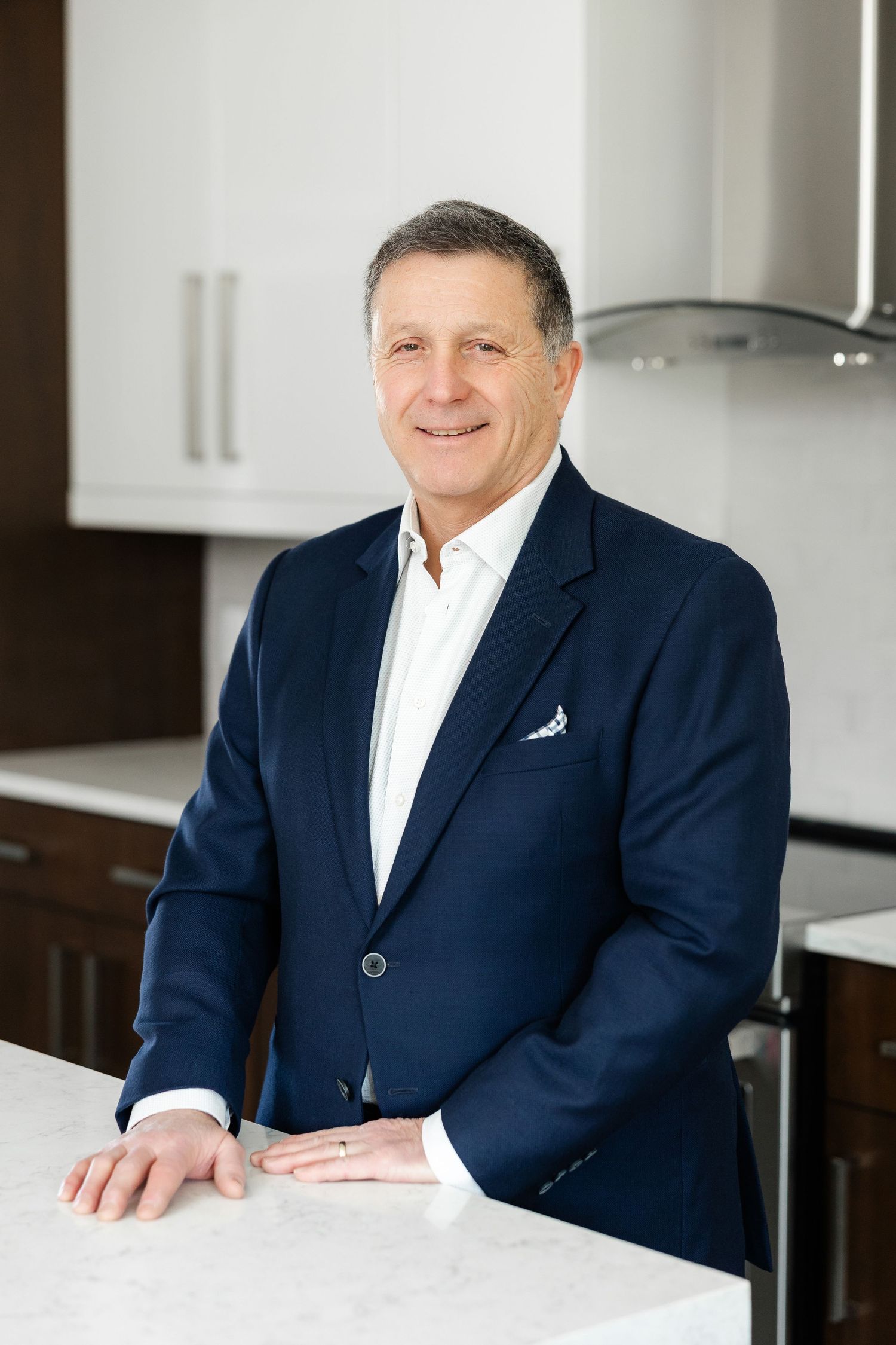 Professional in navy blazer and white shirt standing in modern kitchen.