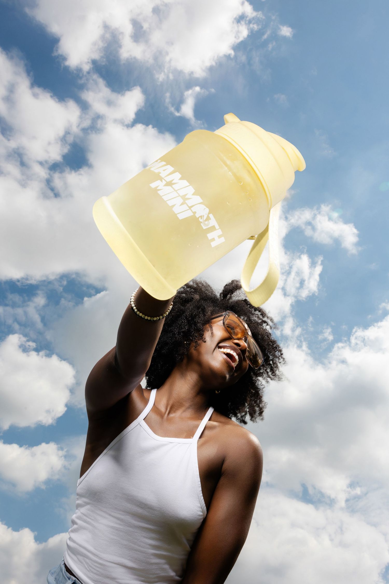 Person in white tank top against blue sky holding yellow container.