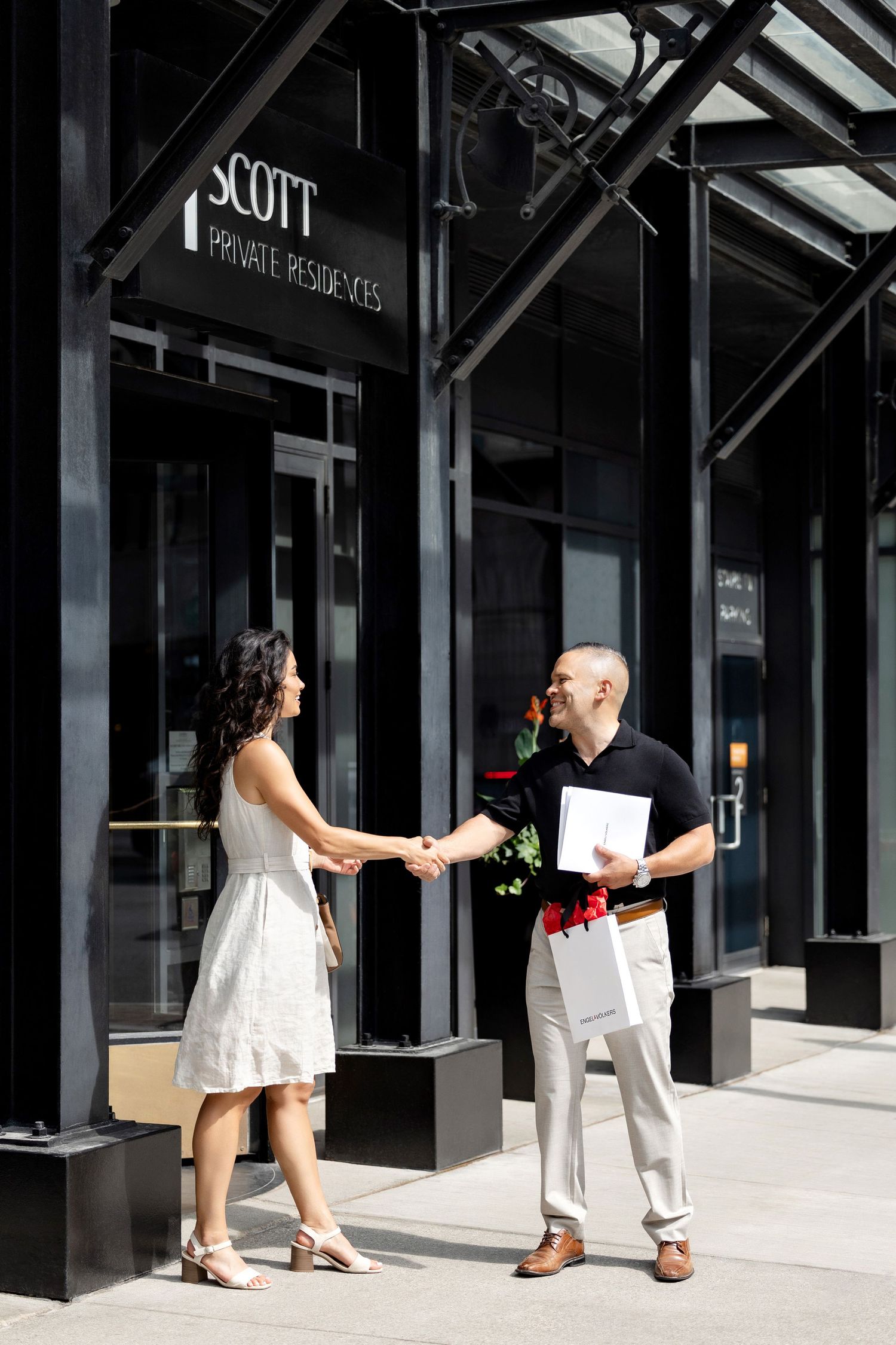Two people exchanging shopping bags in front of retail storefronts.