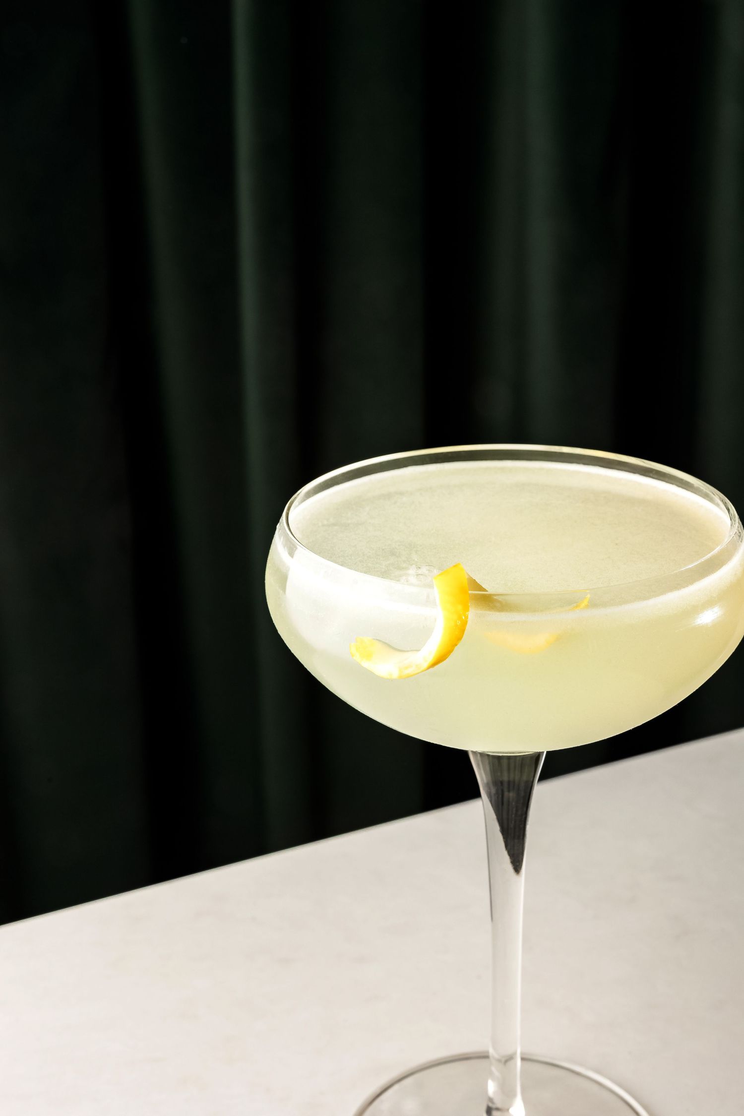Elegant cocktail glass with pale yellow liquid and lemon twist garnish.