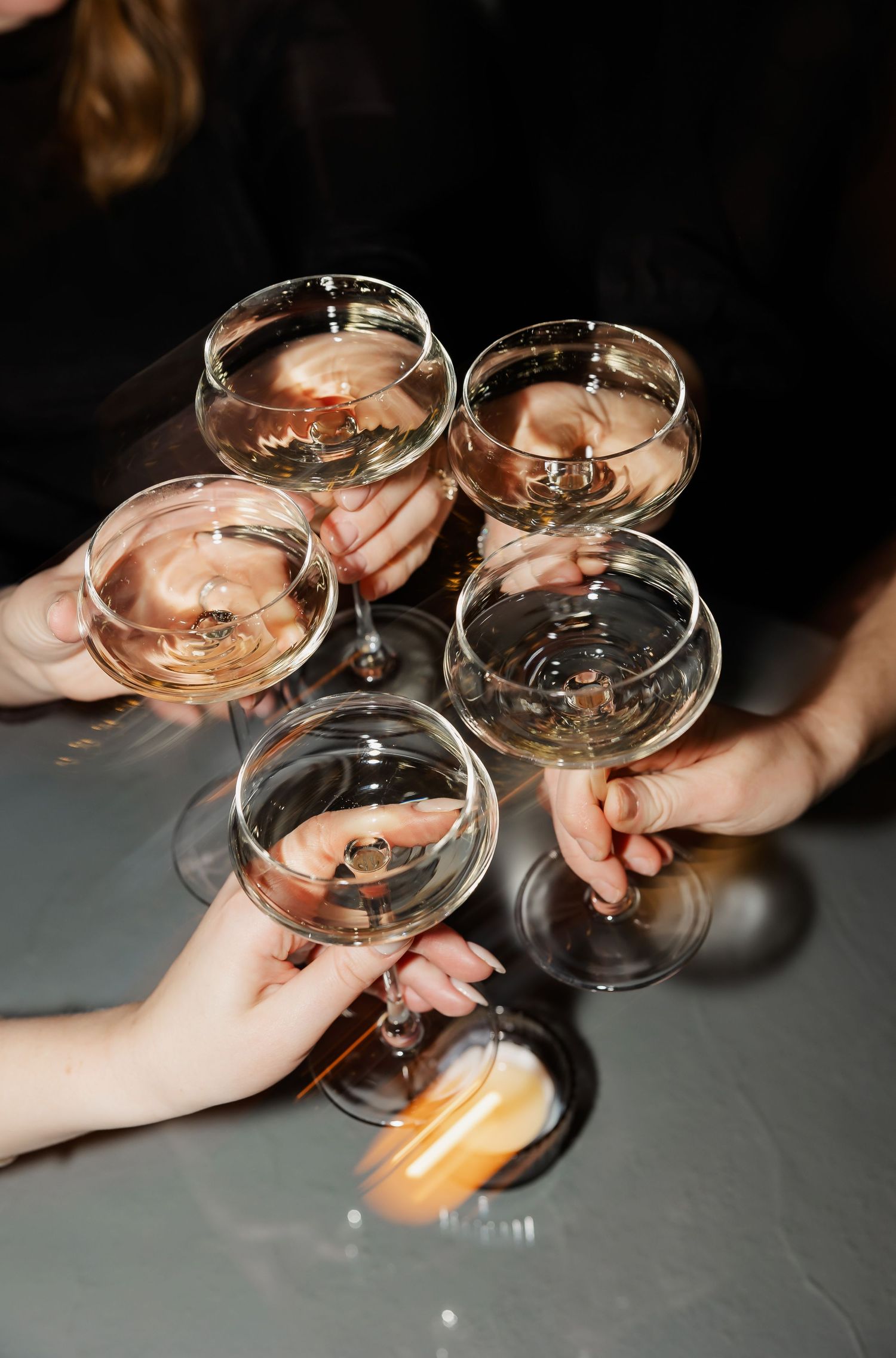 Multiple hands raise wine glasses for a celebratory toast against a dark background.