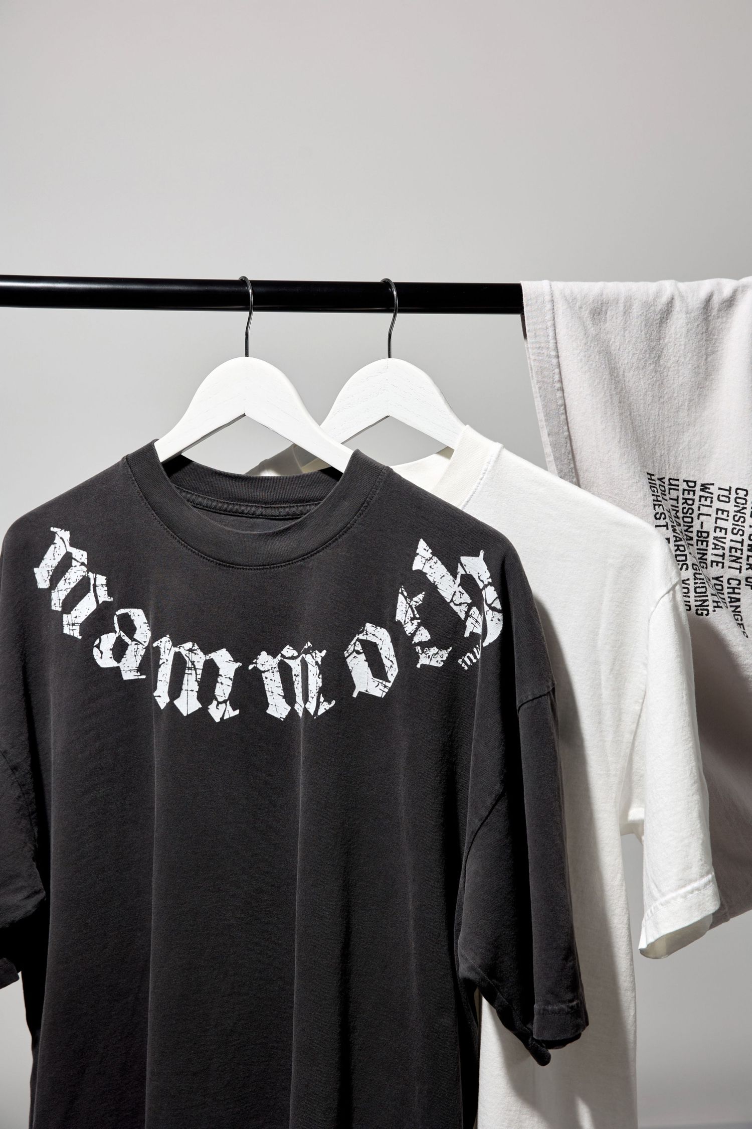 Black and white graphic t-shirts hanging on rack showing gothic lettering designs.