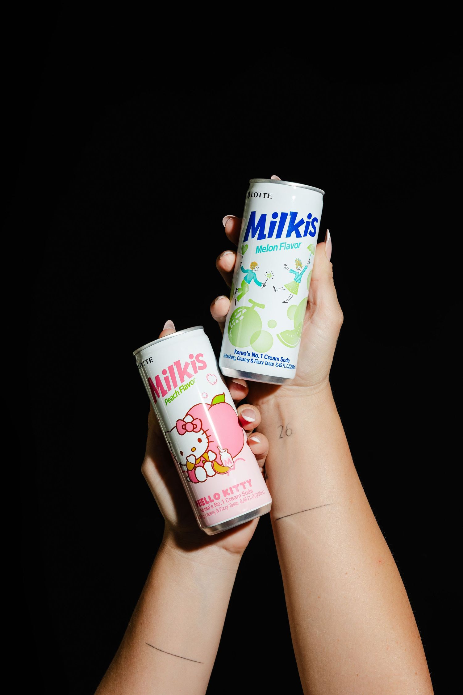 Hands holding colorful cans of Milkis Korean soda drinks against a dark background.