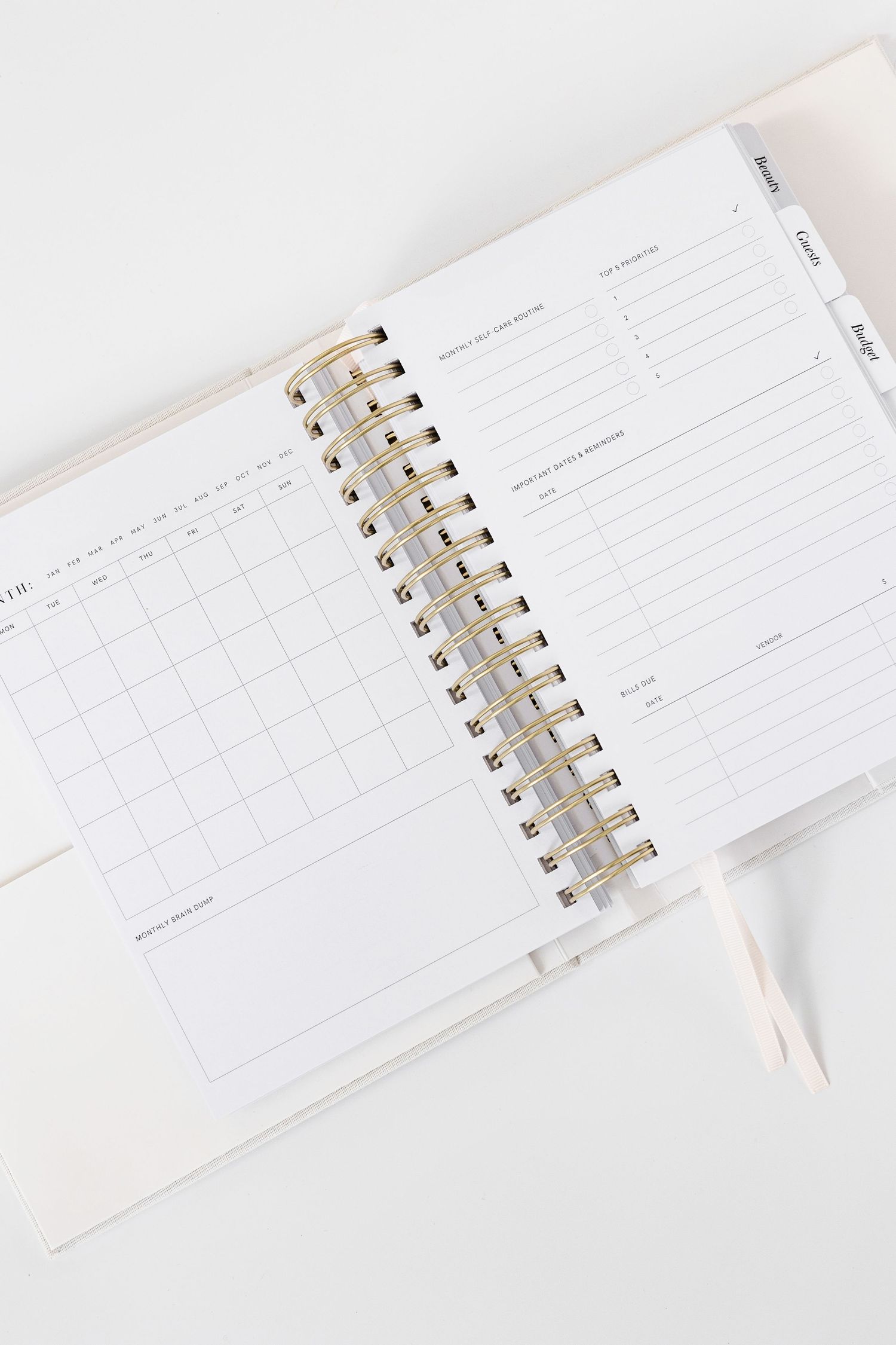 Open white planner showing blank calendar pages with gold spiral binding.