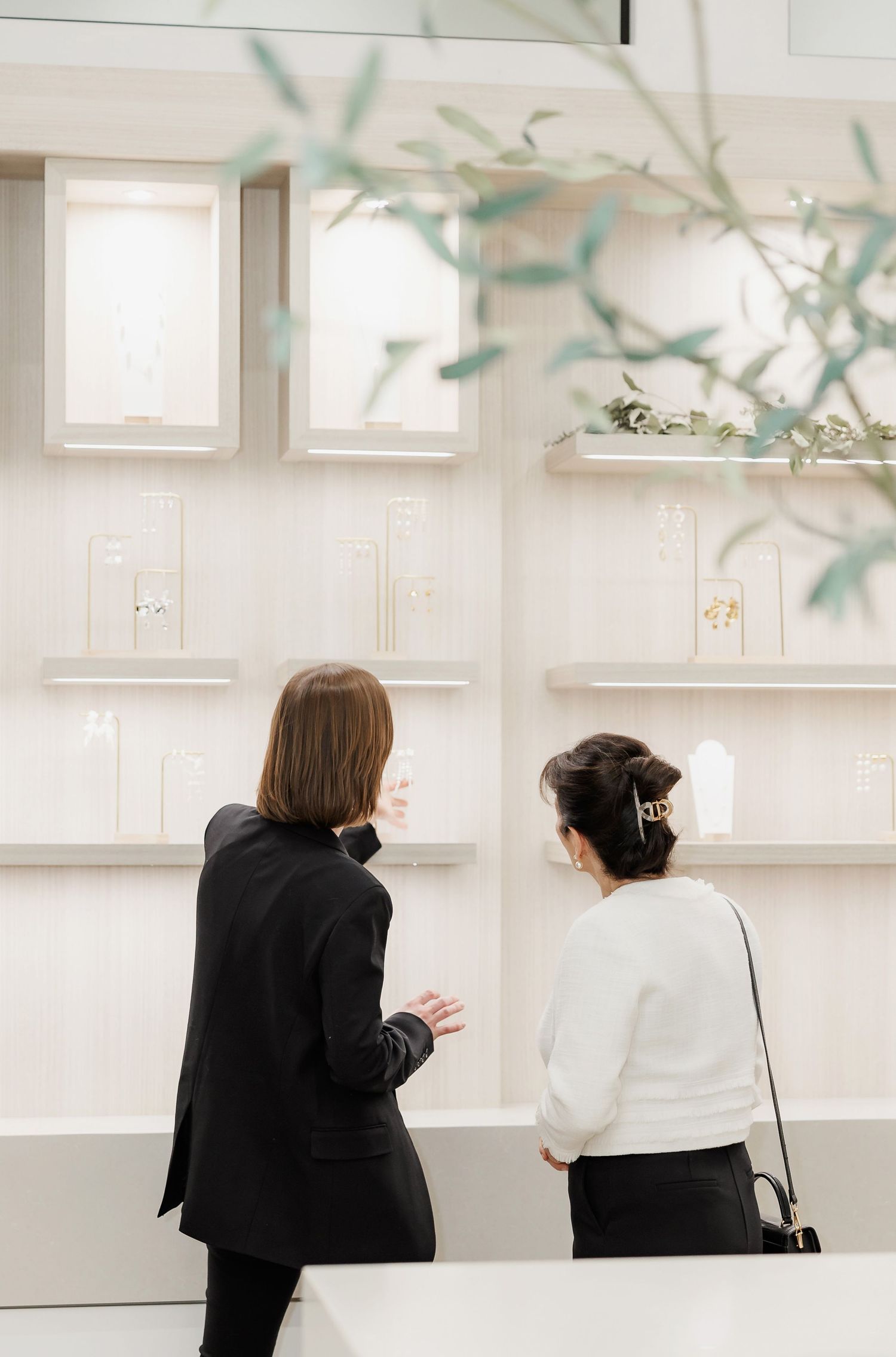 People browse and discuss items at a minimalist white retail display with greenery accents.