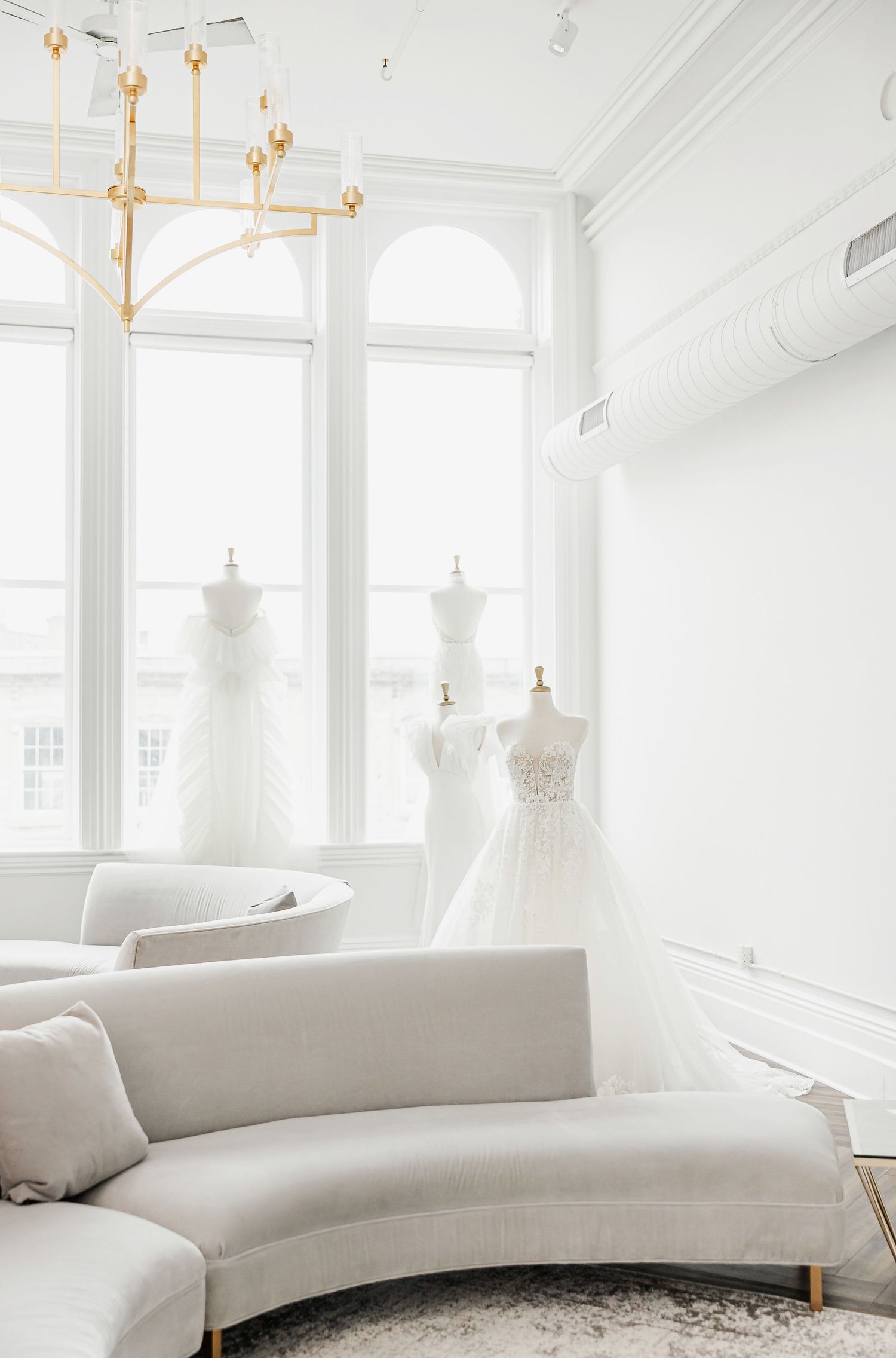 Modern white bridal salon featuring a curved cream sofa and large arched windows.