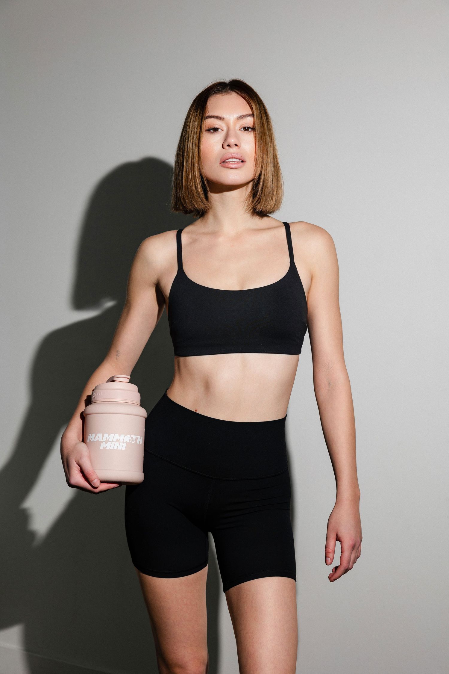 Person wearing black athletic wear demonstrates workout poses with pink container.