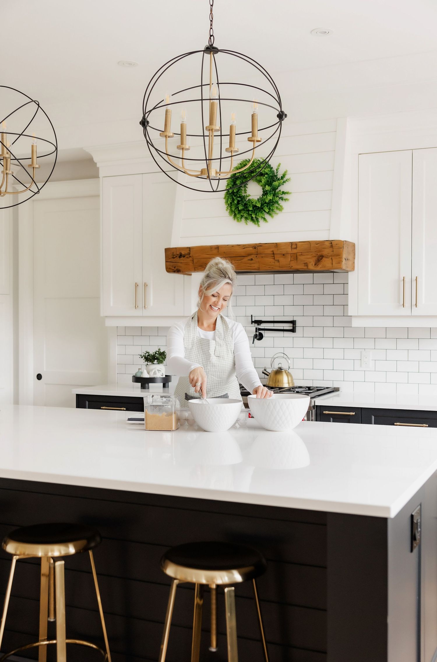 White kitchen featuring black island, geometric chandelier, and subway tile backsplash.