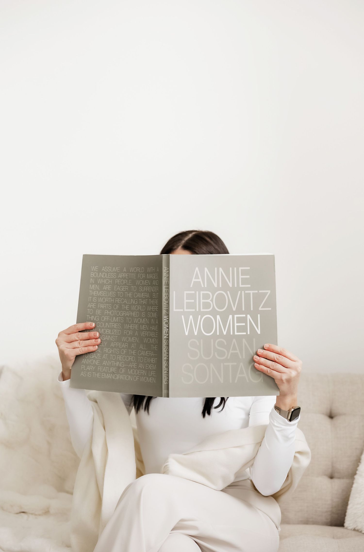 Person reading a photography book while relaxing on a light colored couch.