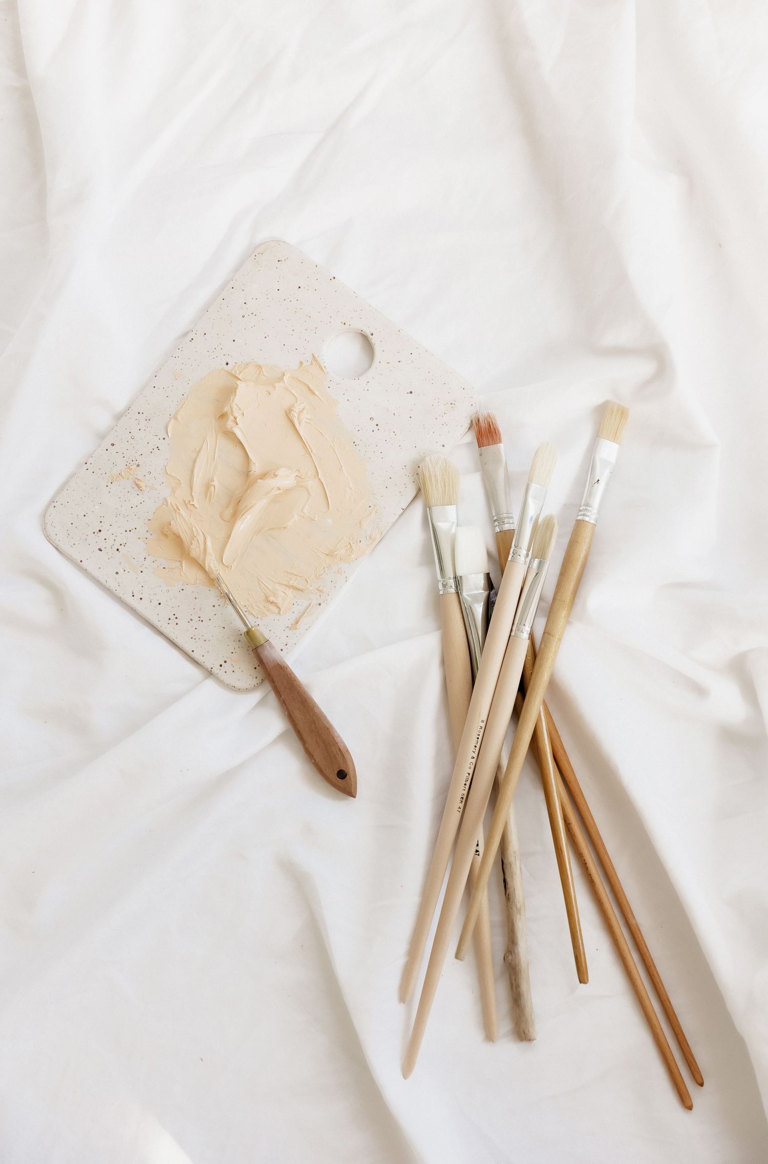 Collection of wooden paintbrushes and art tools arranged on white textile surface.