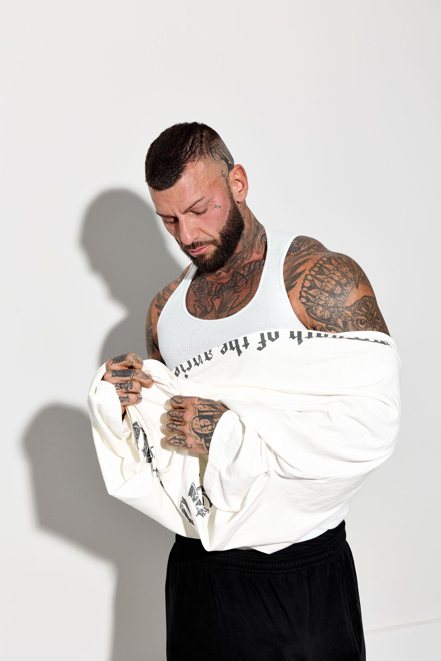 Tattooed person modeling white shirt with text design in various poses.