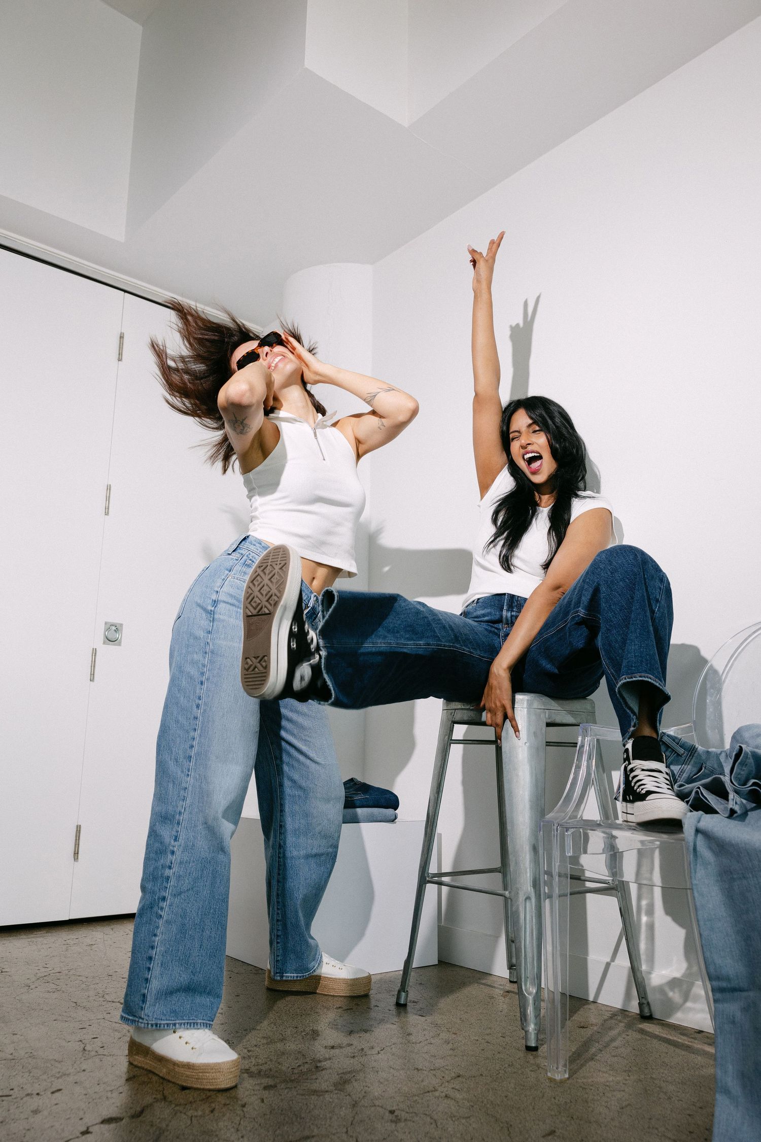 Energetic fashion poses on bar stools showing movement and personality in casual denim outfit.