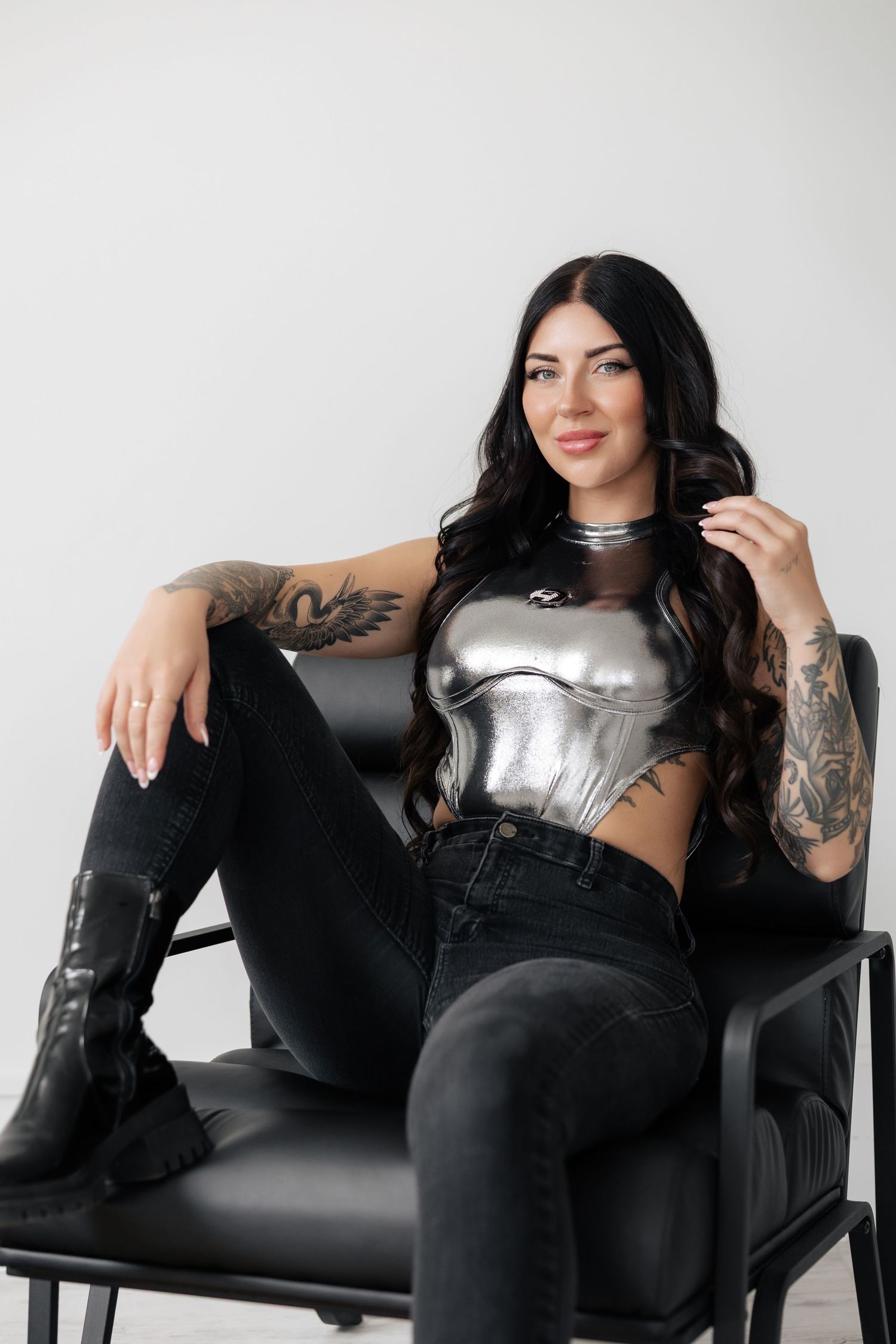 Model lounging on black leather sofa wearing metallic top and dark denim.