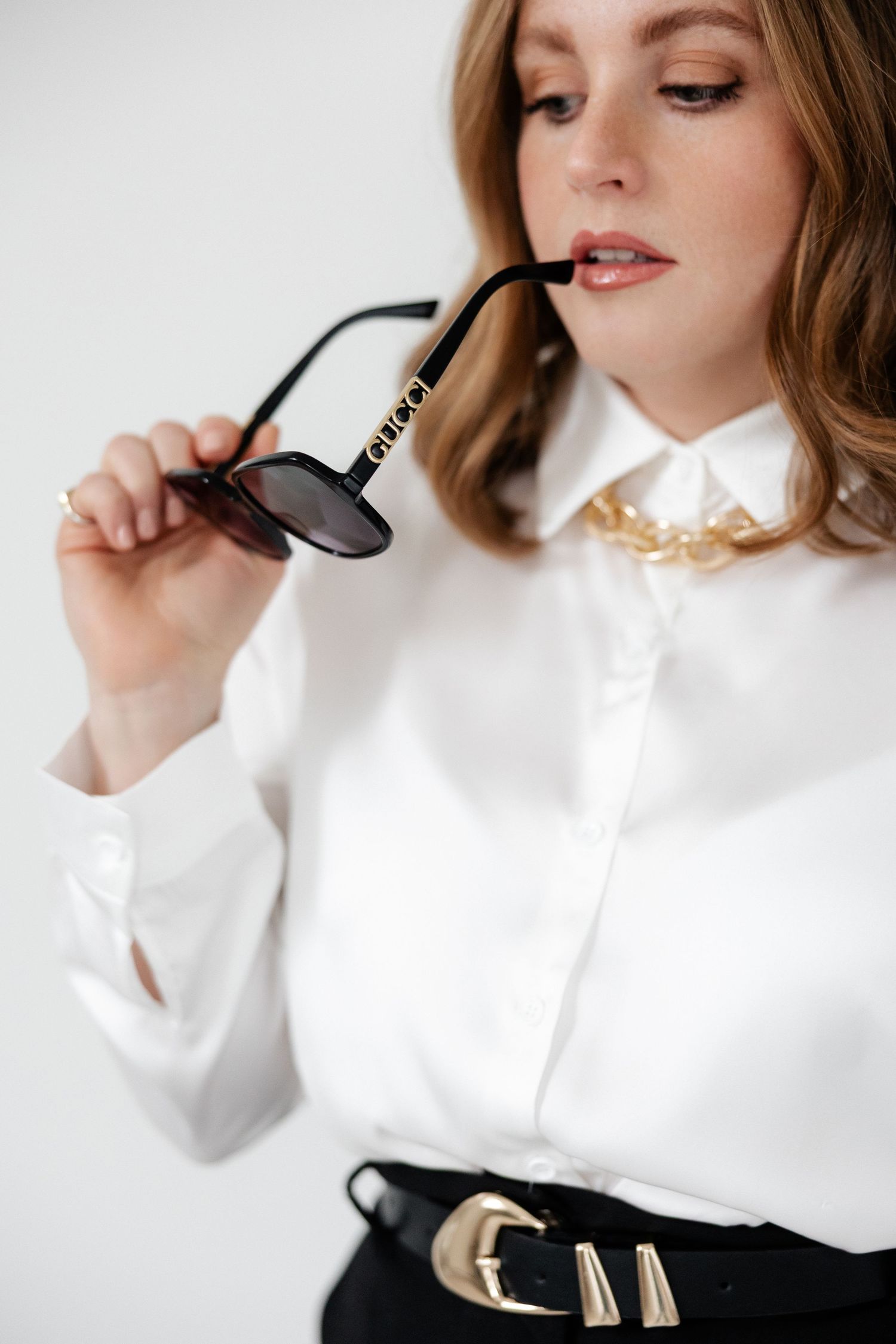 Close-up shot of sunglasses being held against white blouse with gold collar detail.