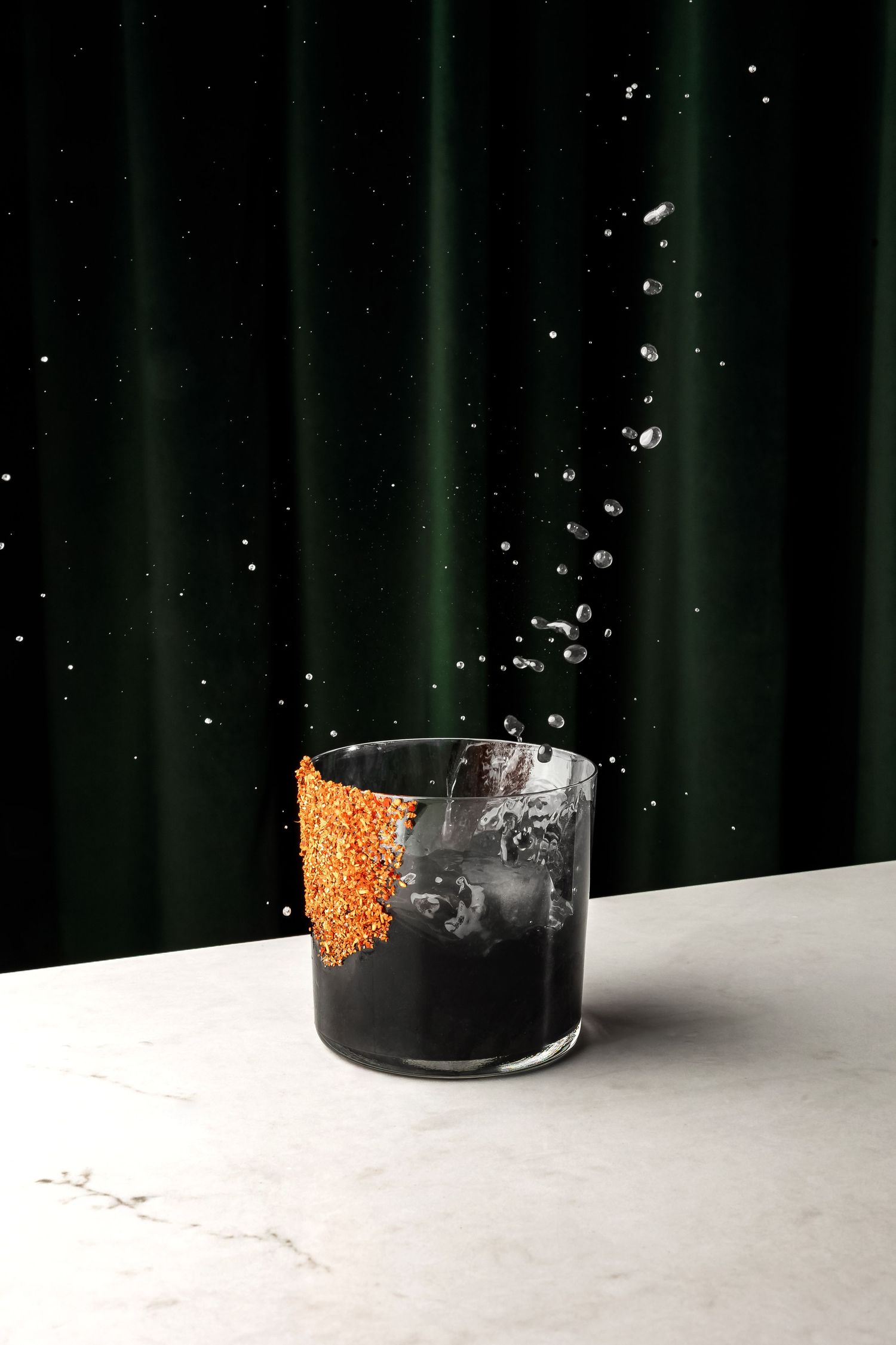 Orange fish roe creating a splash in black liquid on white surface.