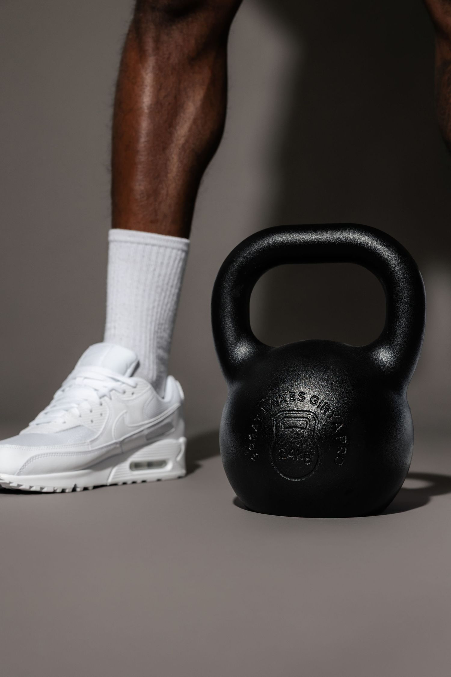 Black kettlebell next to white athletic shoe and sock against grey background.