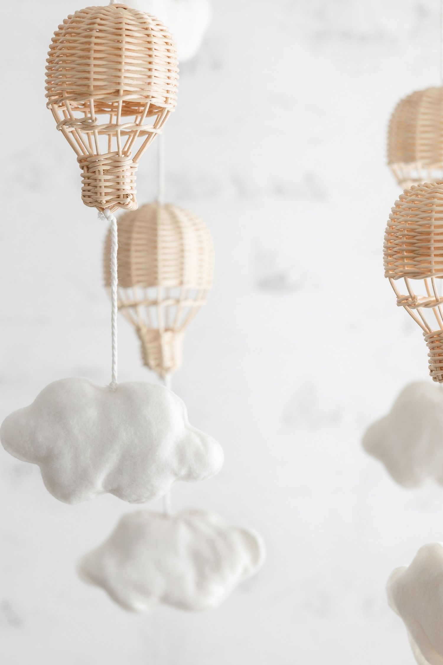 Delicate woven rattan hot air balloon mobile with white cloud decorations against a light background.