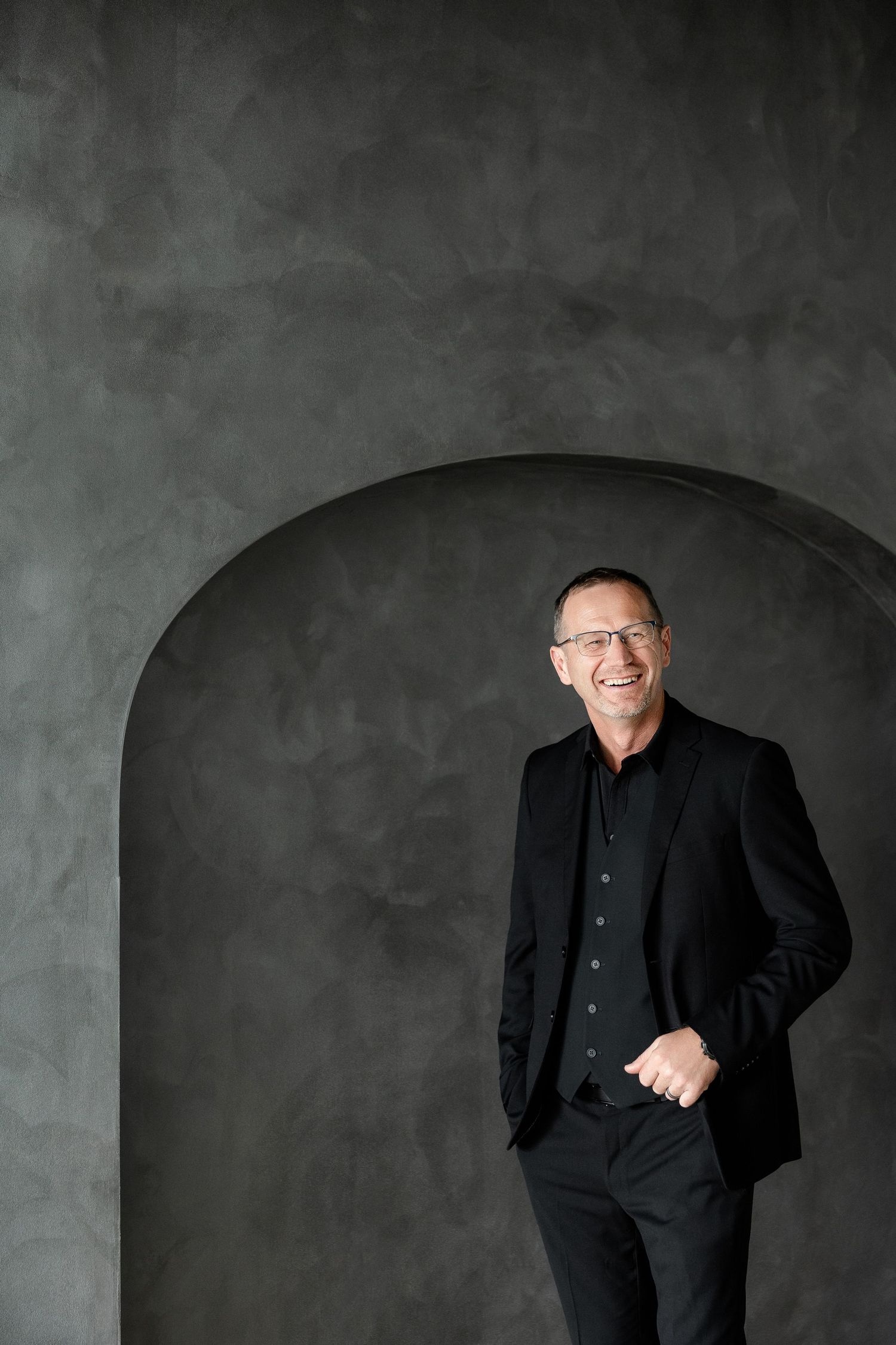 Professional wearing all black poses against textured grey backdrop in multiple shots.