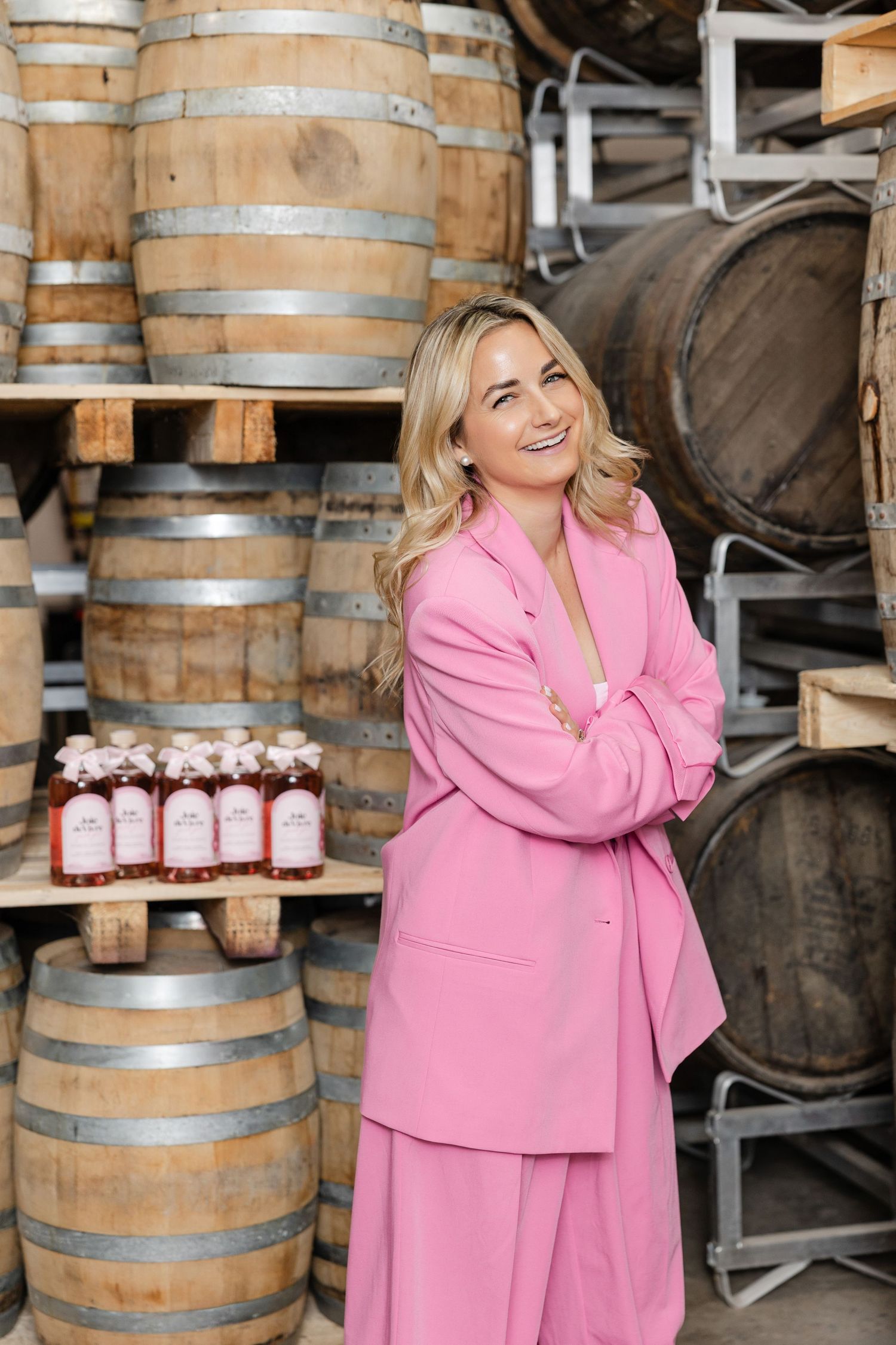 Pink-suited figure standing near wooden wine barrels in cellar.