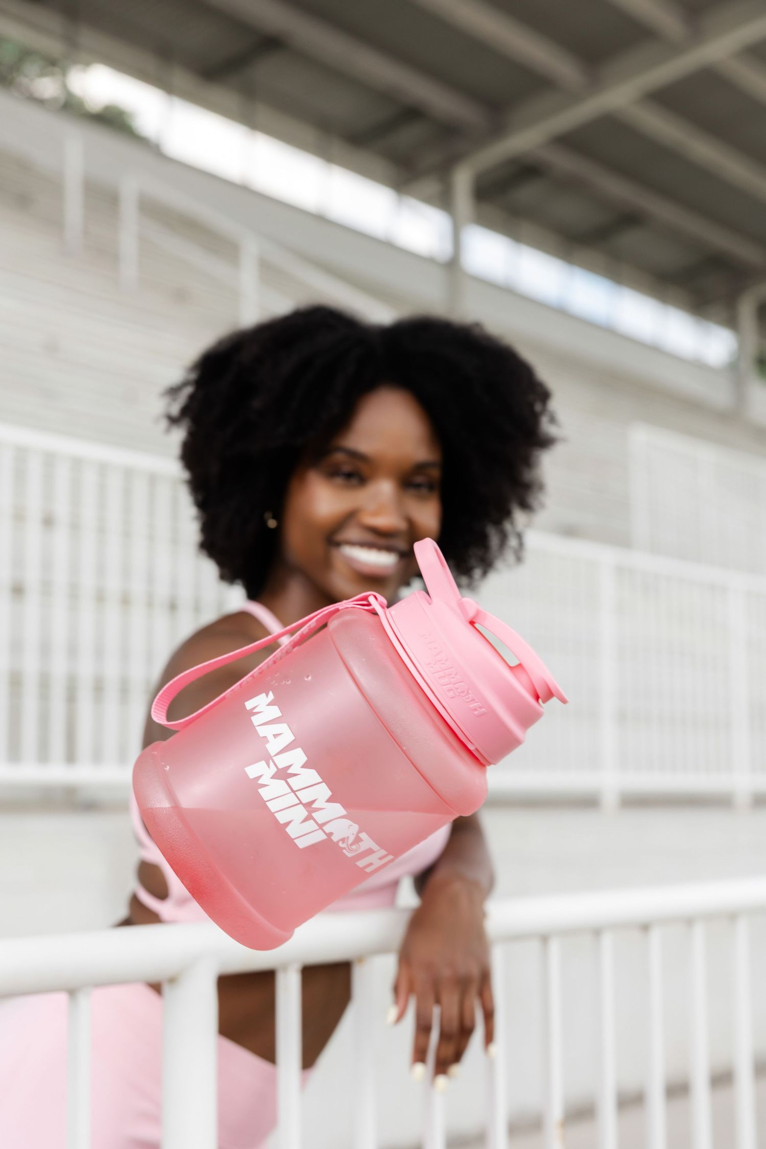 Woman in pink athletic wear smiling while holding pink water bottle.