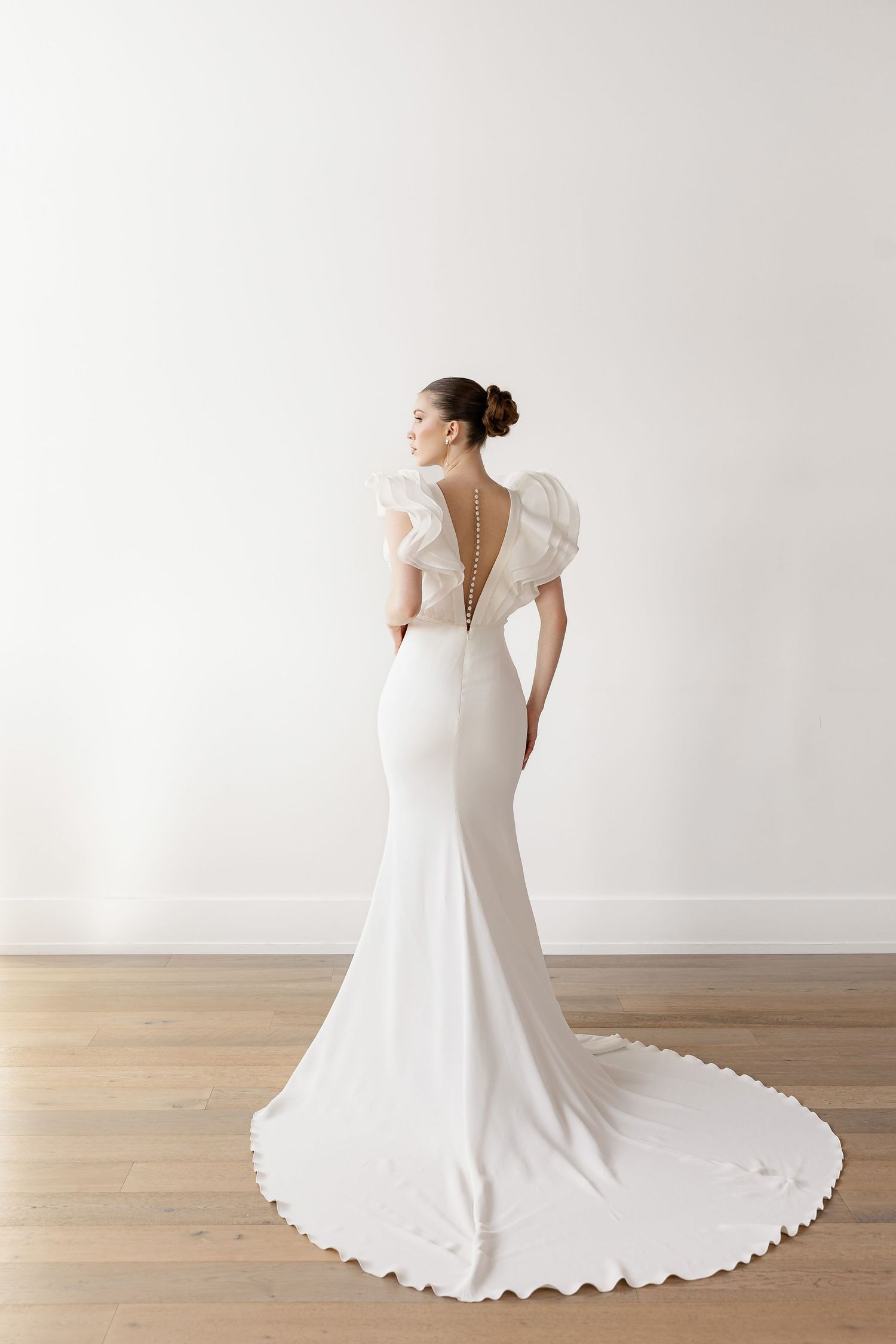 Elegant fitted wedding gown with dramatic train and ruffled cap sleeves on wooden floor.